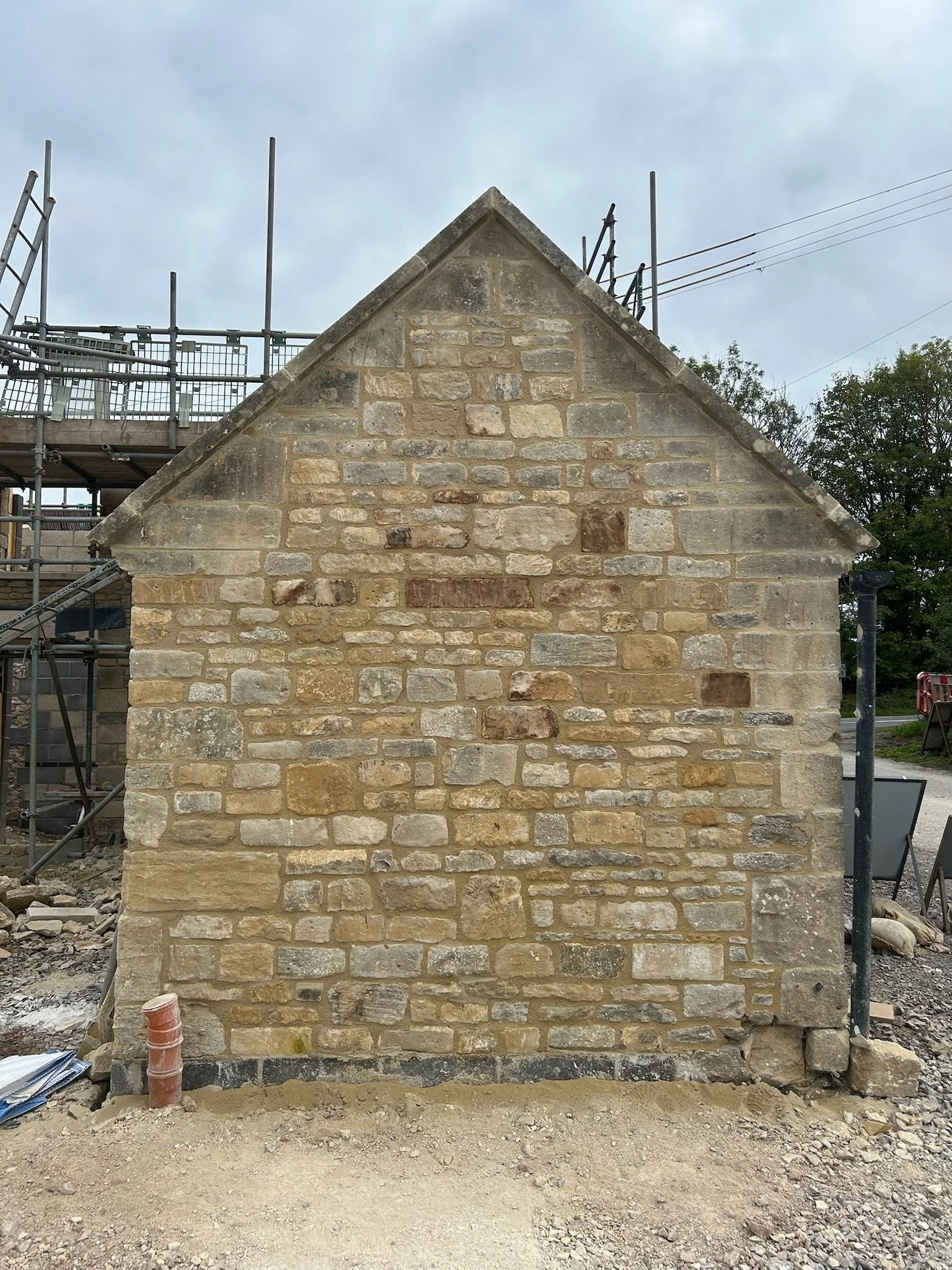Close-up of a stone building under construction or renovation, with scaffolding on the left side and a cloudy sky above.