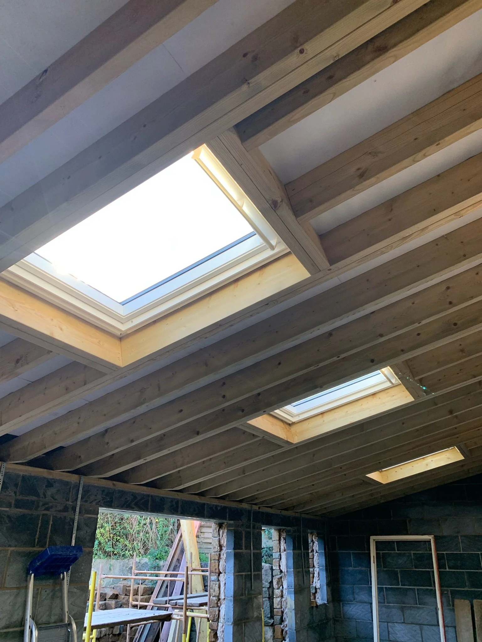 Construction of a building ceiling with skylights, showing wooden beams and the skylights installed in the roof.