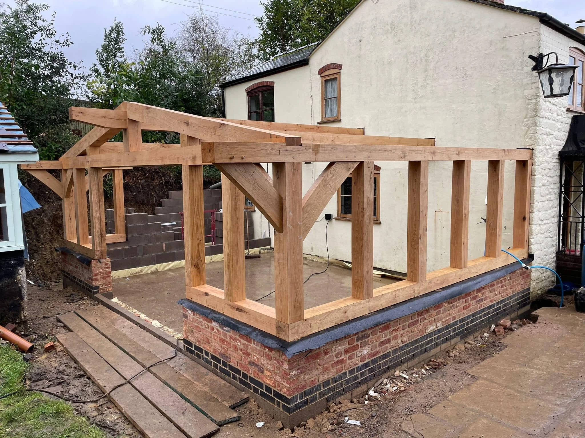 Wooden framework construction on a brick foundation, attached to the side of a house.