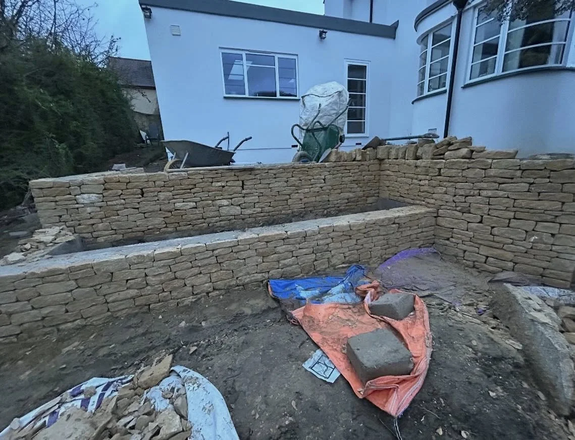 Under construction stone wall in a backyard with tools and building materials