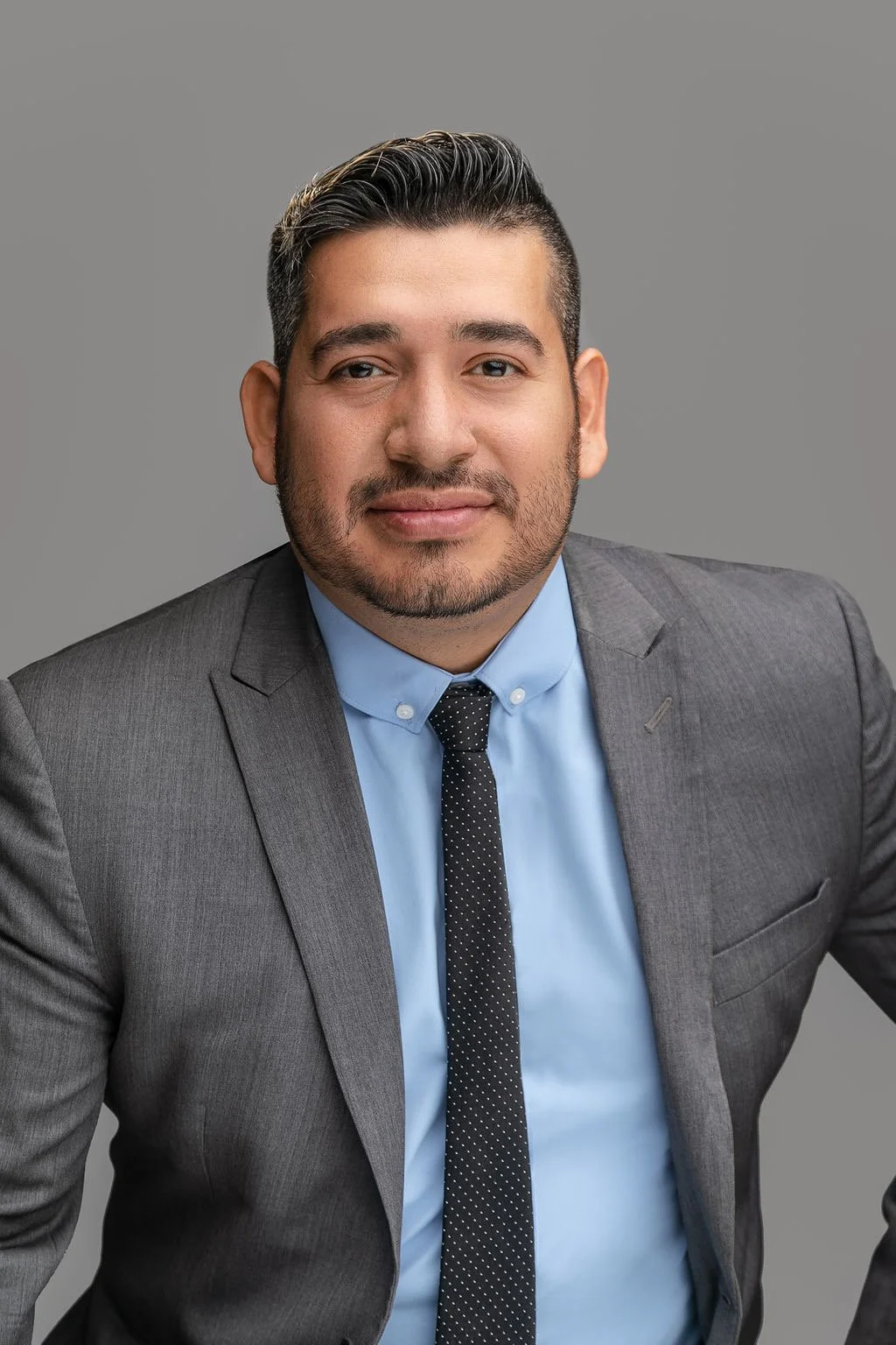 Headshot of a man with dark hair, beard, wearing a gray suit, light blue shirt, and black dotted tie, against a gray background. Life insurance broker, retirement strategist