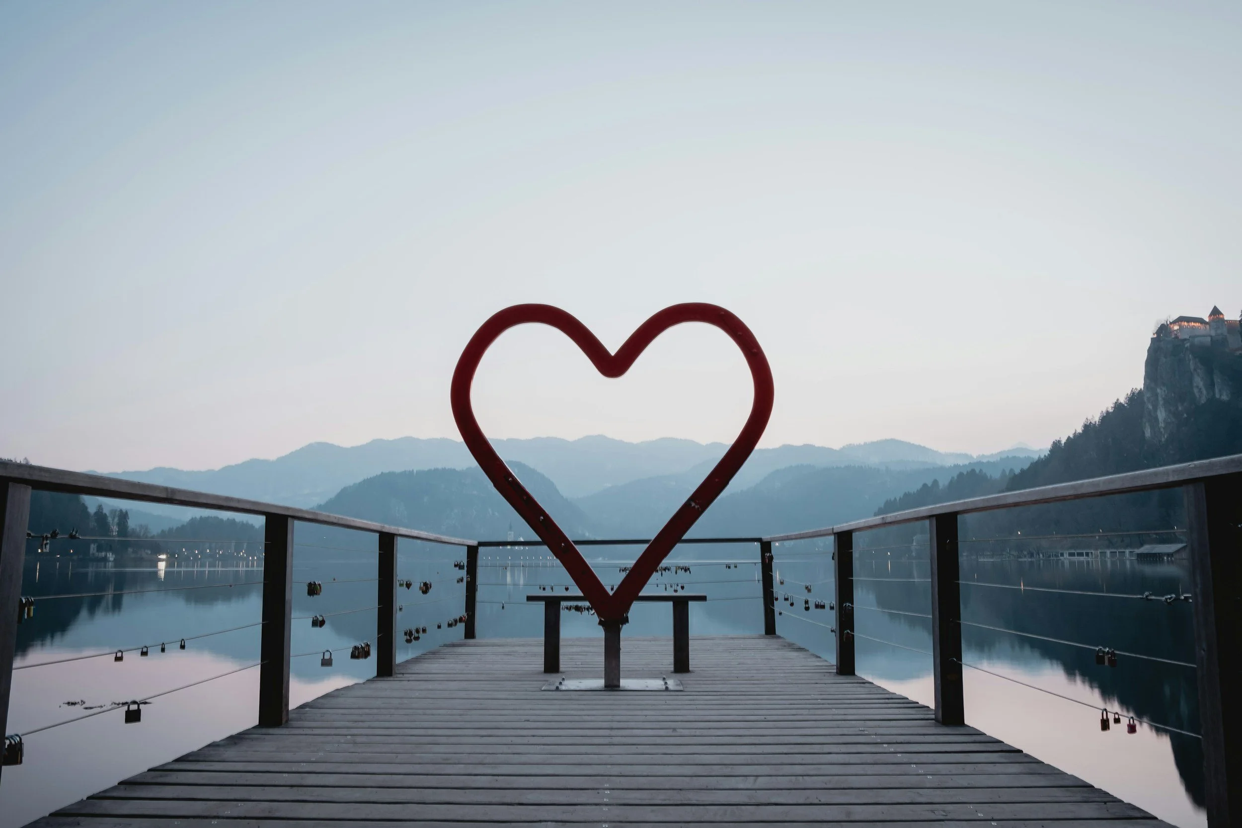 heart structure on a pier overlooking water and the mountains