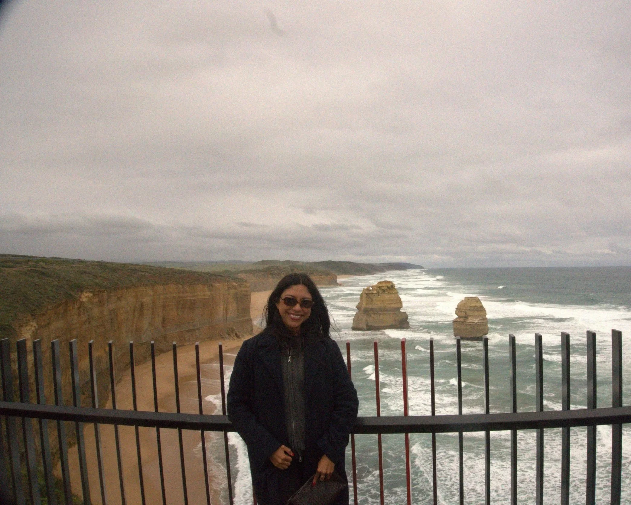 Girl in sunglasses and a sweater smiling in front of the 12 Disciples rock formation on the Great Ocean Road in Australia.