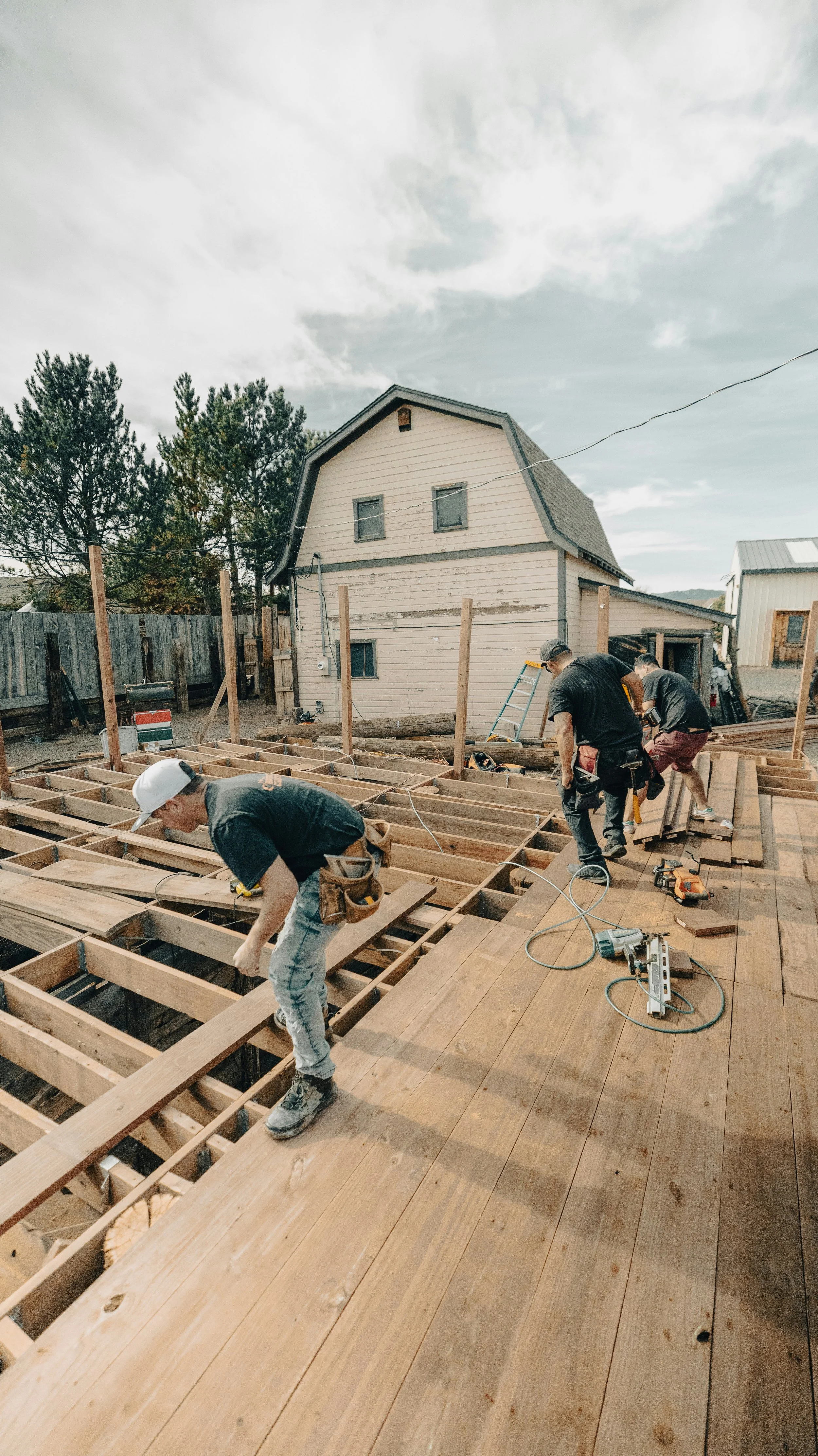 Construction workers building a wooden deck outside a house, with tools and materials on site.