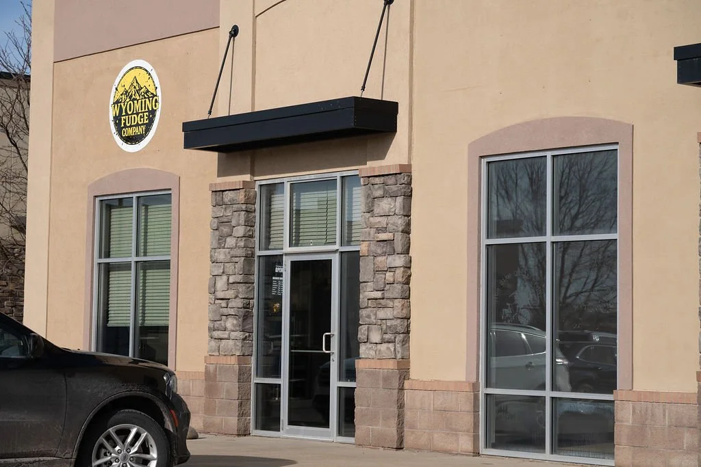 Exterior of Wyoming Fudge Company storefront with stone accents around glass door and large windows, and a Wyoming Fudge Company sign on the wall.