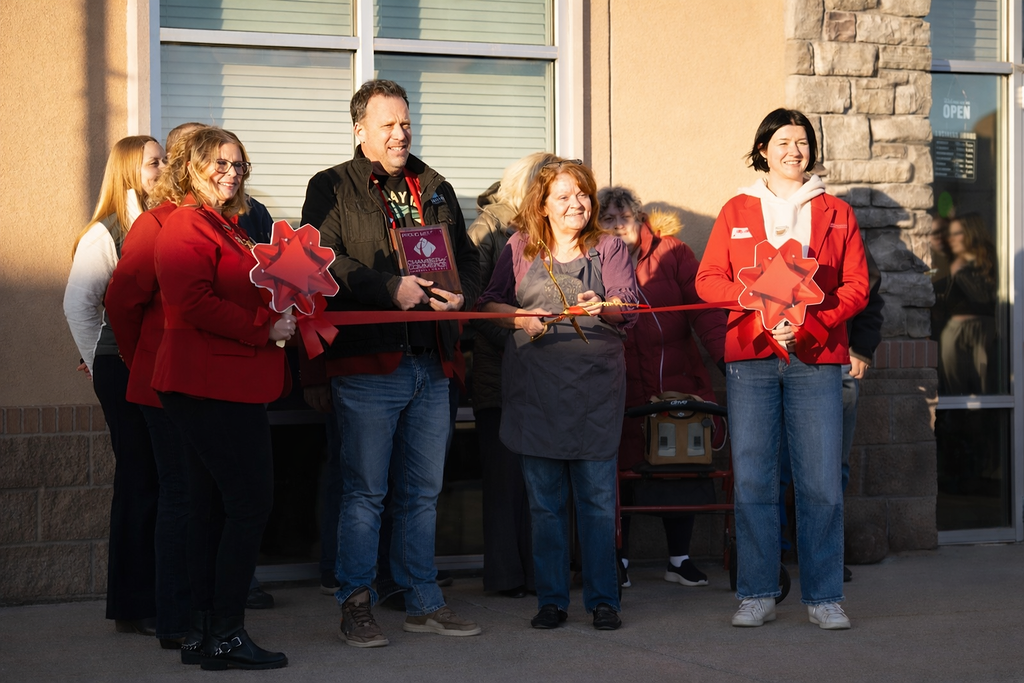 Group of people at a ribbon-cutting ceremony outside a building, holding large decorative scissors and smiling.