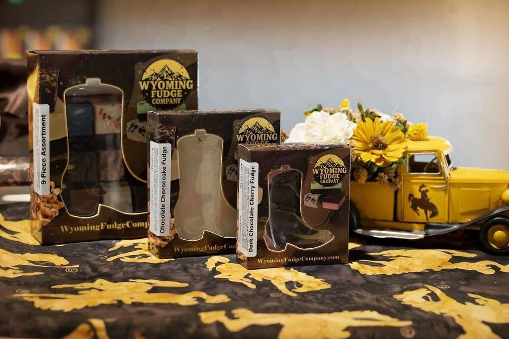 Three boxes of Wyoming Fudge Company assorted chocolates, a yellow vintage truck planter with white and yellow flowers, on a black and yellow Wyoming-themed tablecloth.