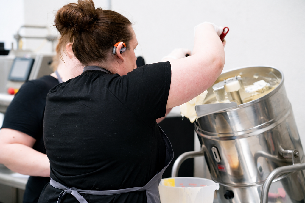 A woman operating a large industrial gelatin or candy melting machine in a commercial kitchen.