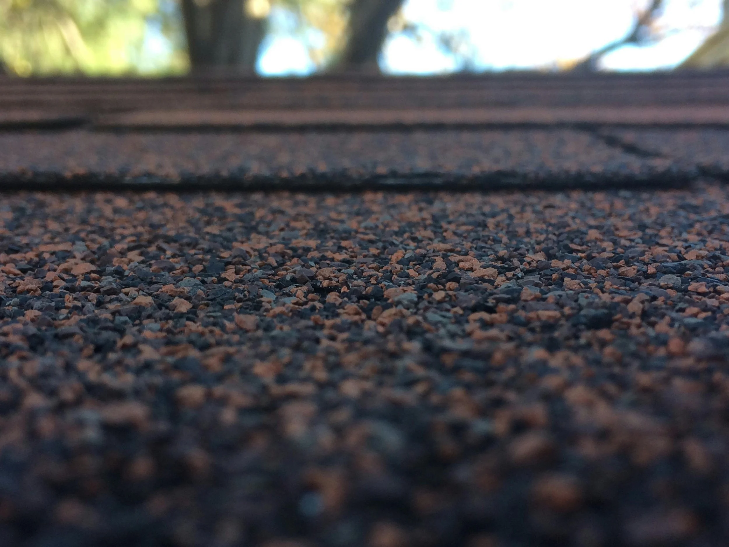 Close-up of a gravel surface with a blurred view of a branch and sky in the background.