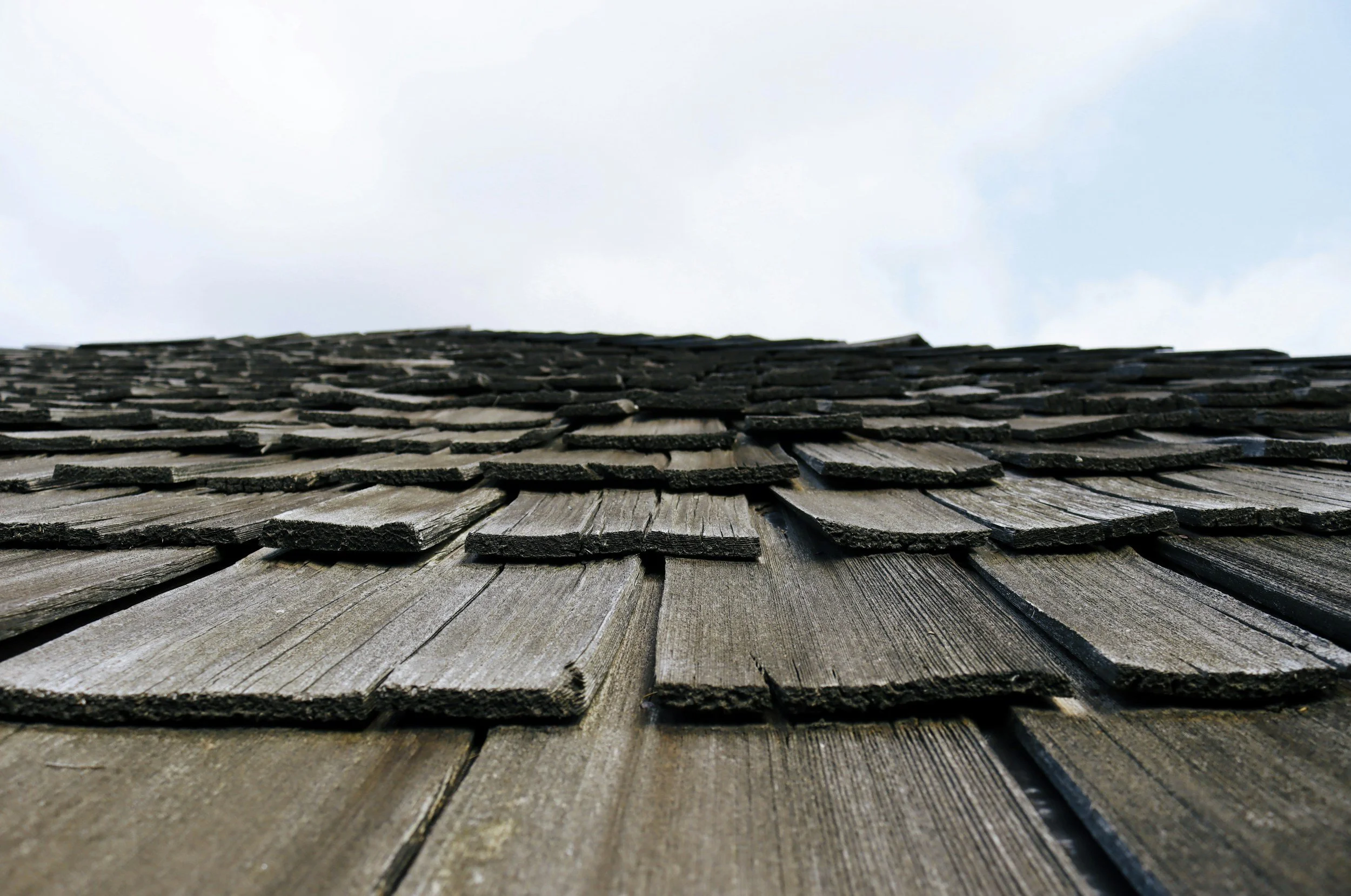 Close-up view of weathered wooden shingles on a roof, looking upward towards the sky.