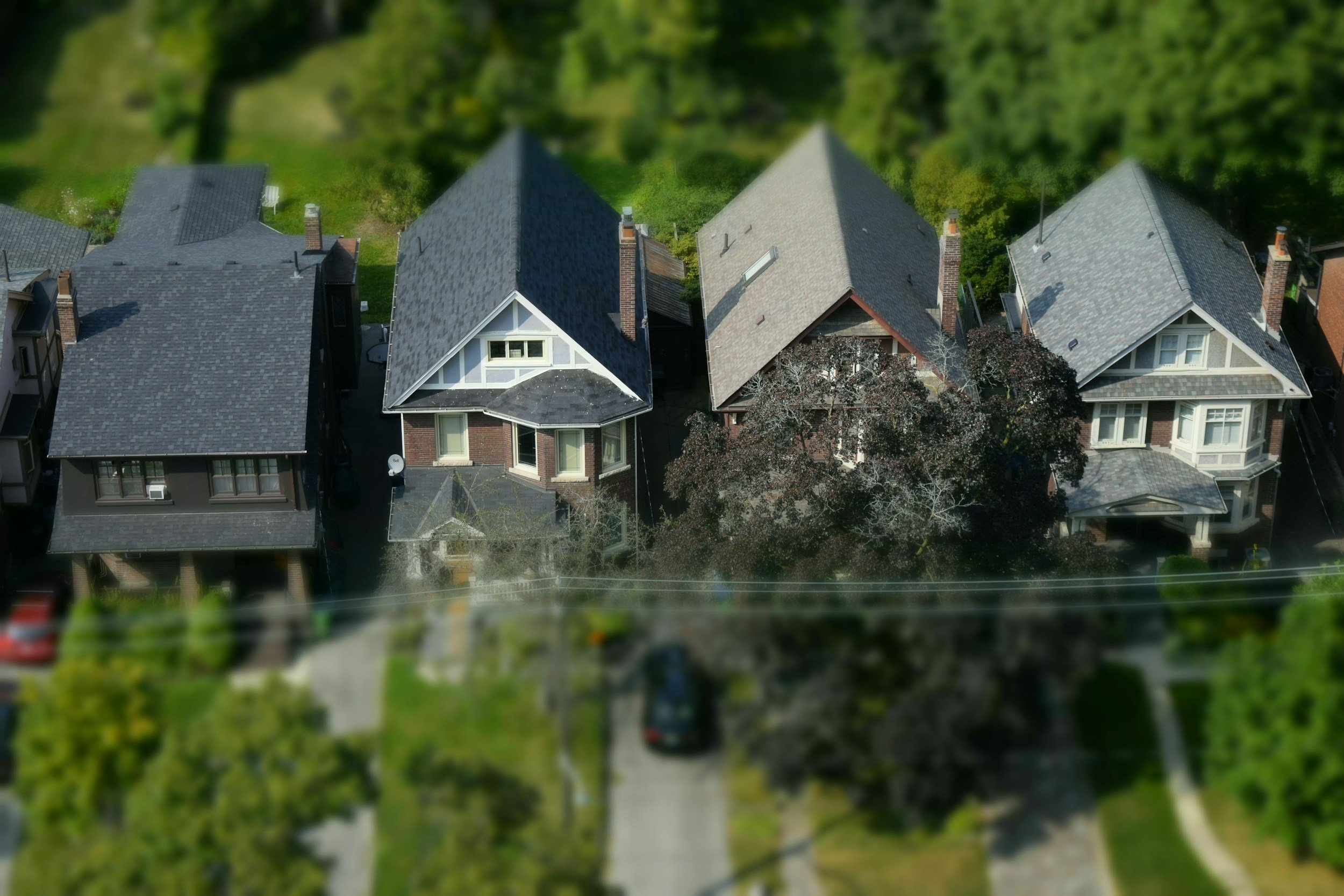 Aerial view of three houses in a neighborhood, surrounded by trees and greenery.