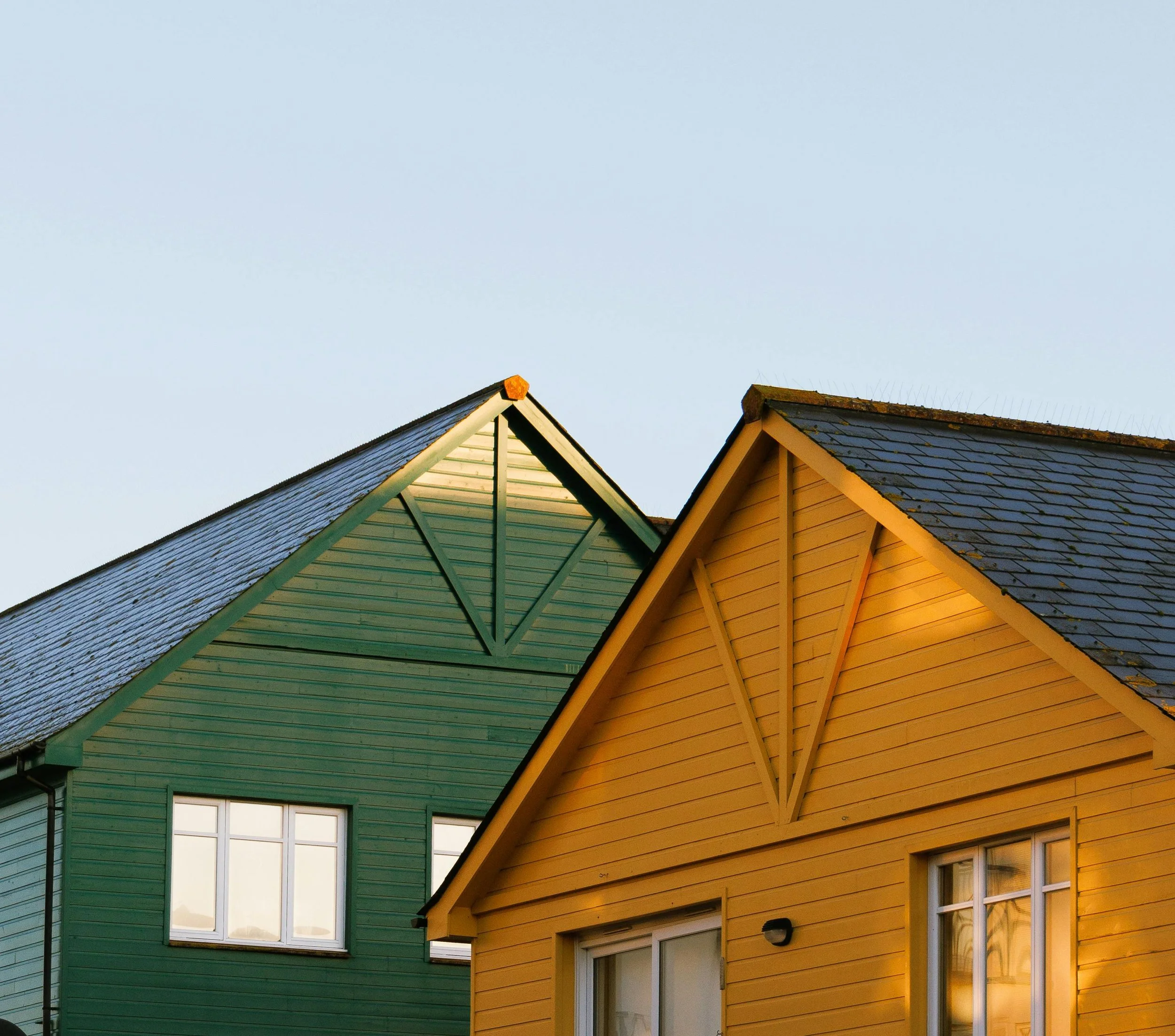 Two colorful houses with pointed roofs, one green and one yellow, under a clear blue sky.