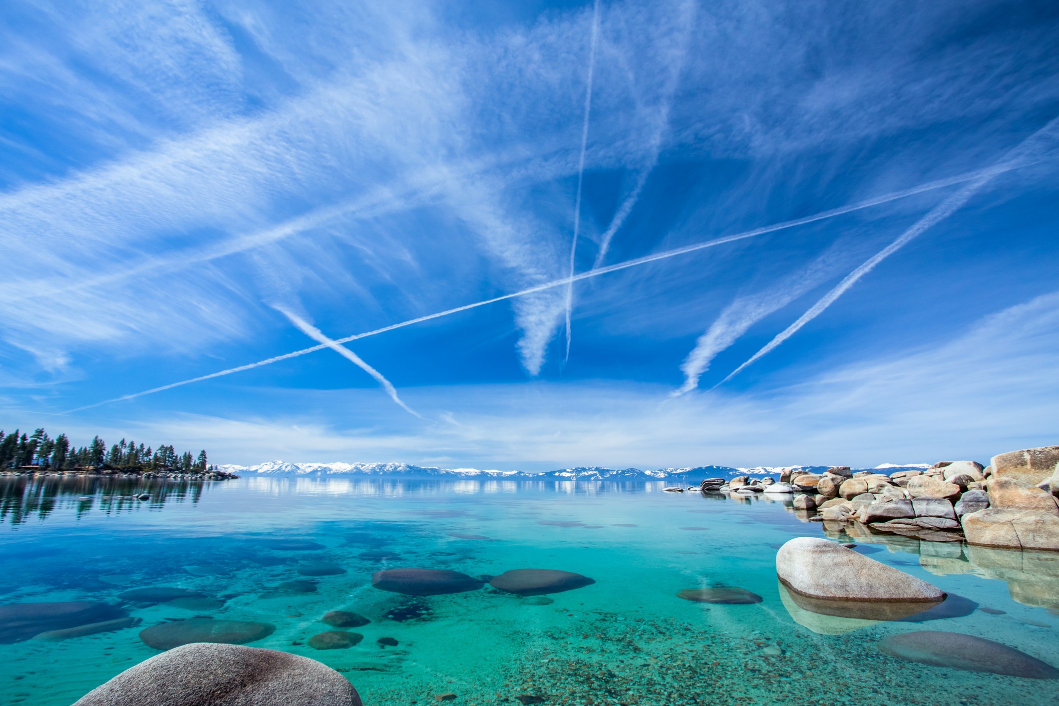 A bay in, Lake Tahoe, Nevada with private jet contrails in the sky.