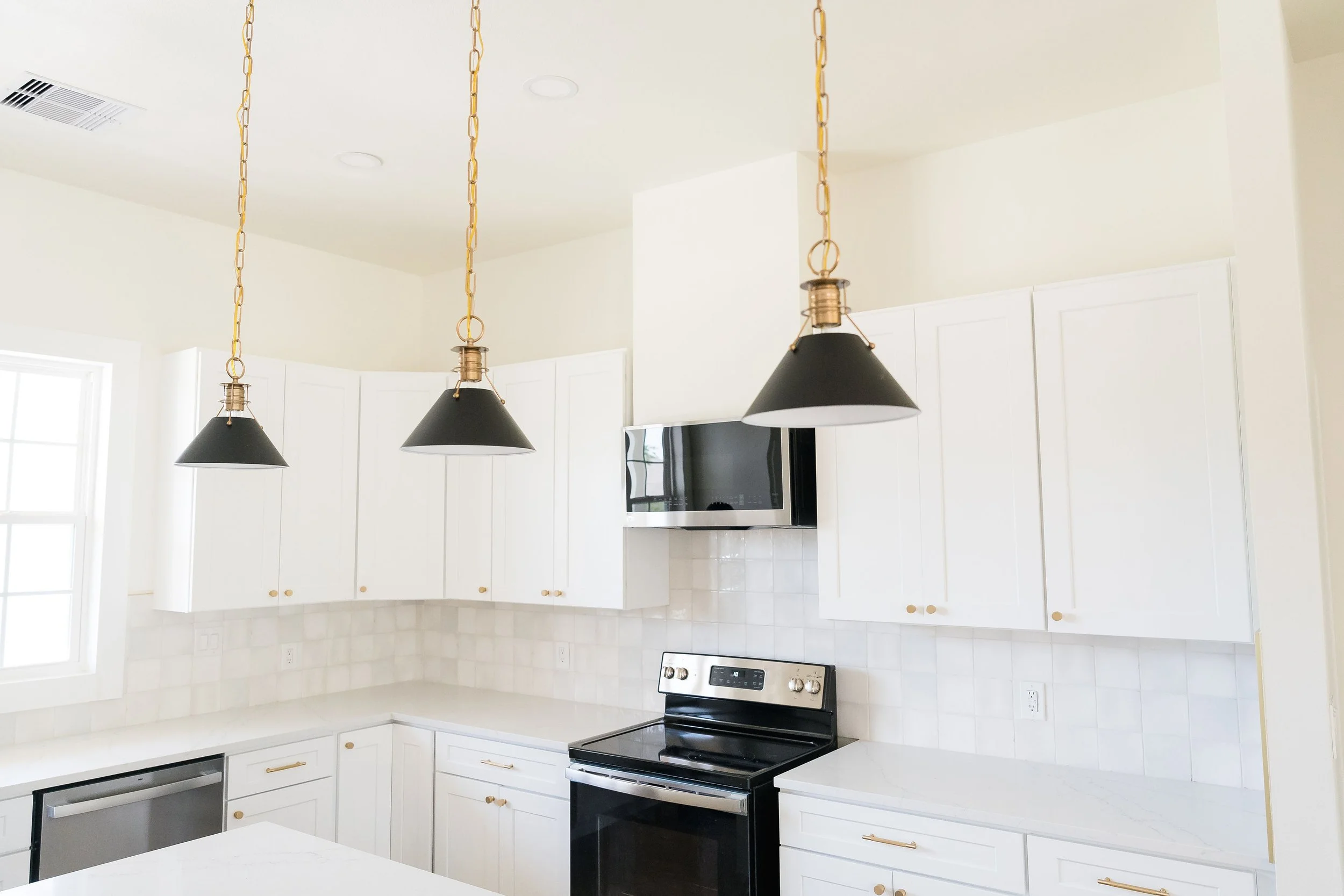Modern kitchen with white cabinets, black stove, black microwave, and three black pendant lights with gold chains hanging from the ceiling.