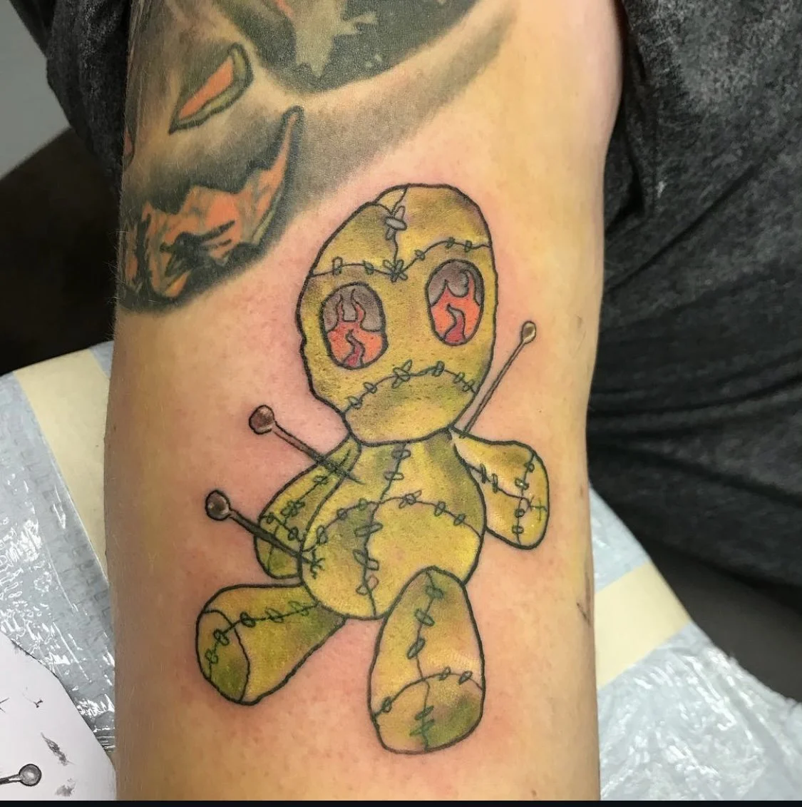 Teddy bear tattoo with yellow and black colors, stitched with string, and having red eyes.
