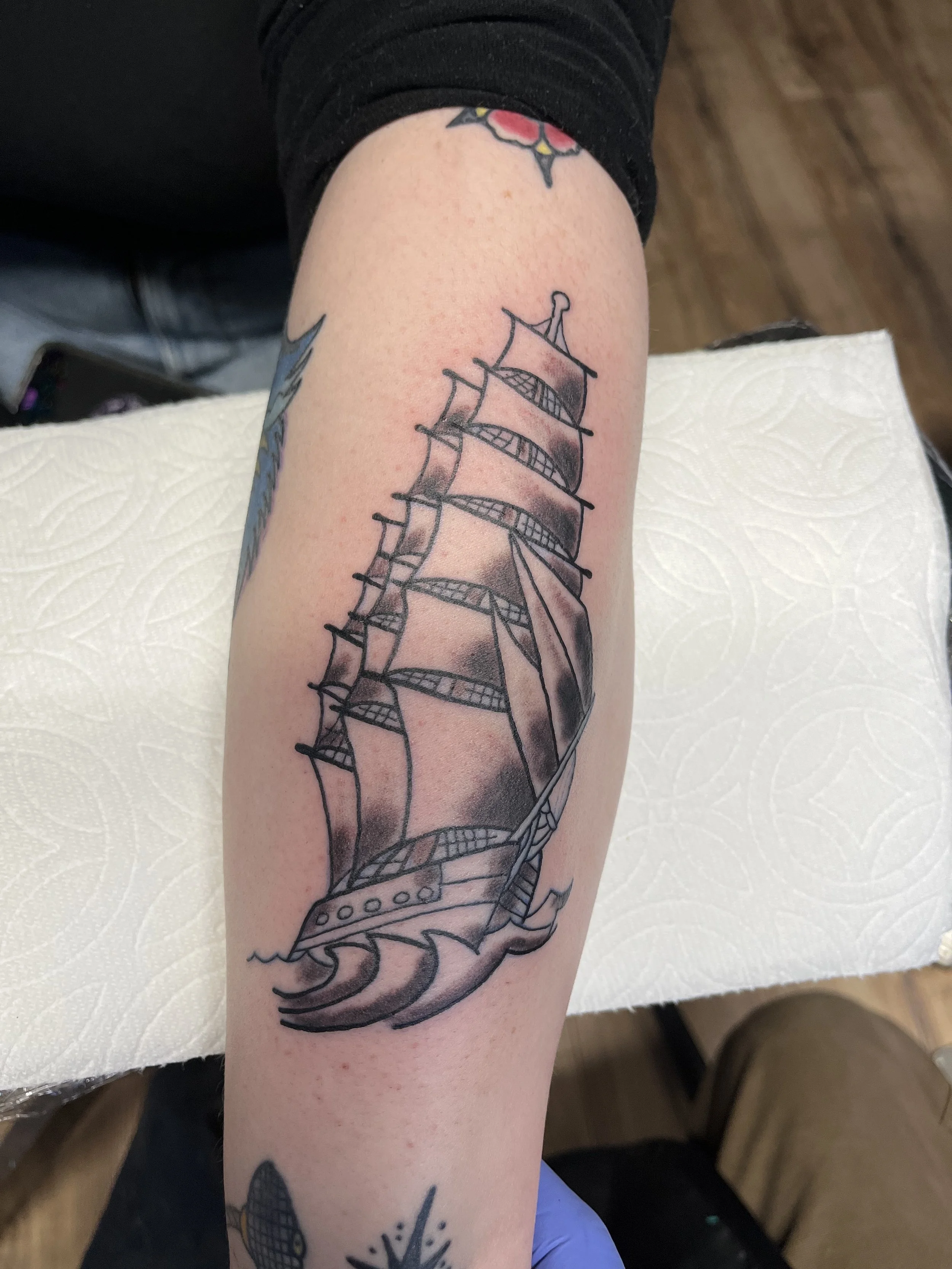 Tattoo of a sailing ship with billowing sails on a person's forearm.