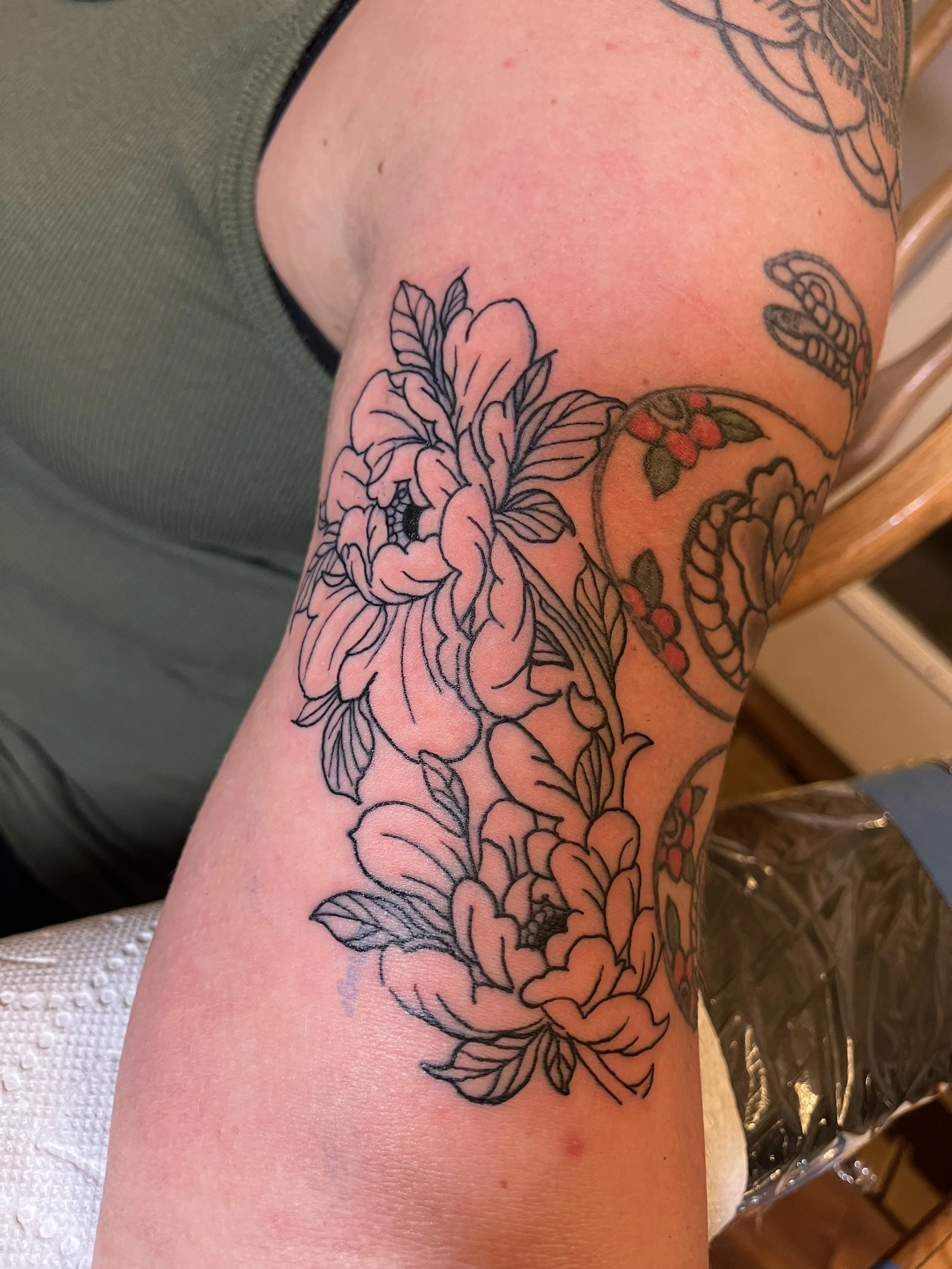 Outline tattoo design of flowers and leaves on a person's arm.