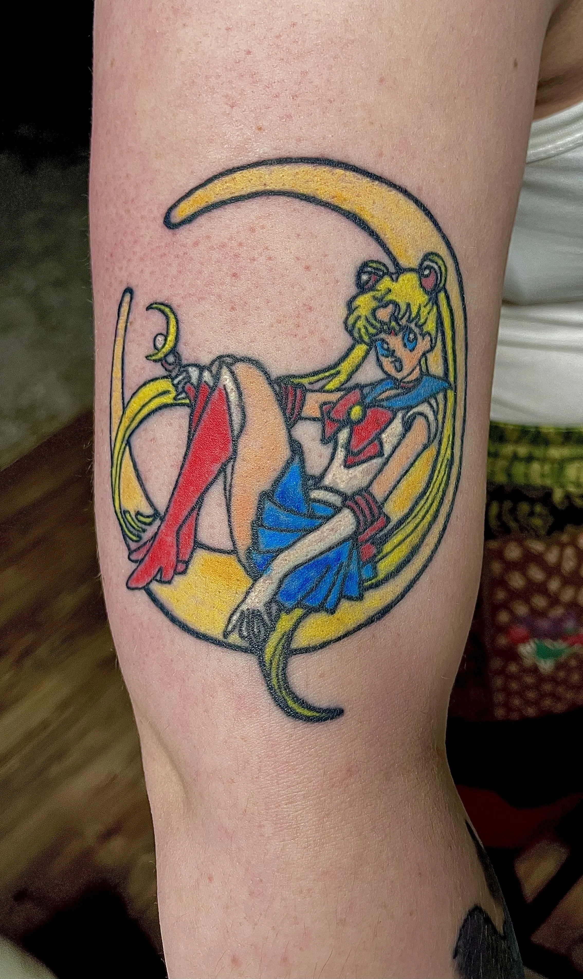 Tattoo of Sailor Moon sitting on a crescent moon surrounded by a yellow frame.