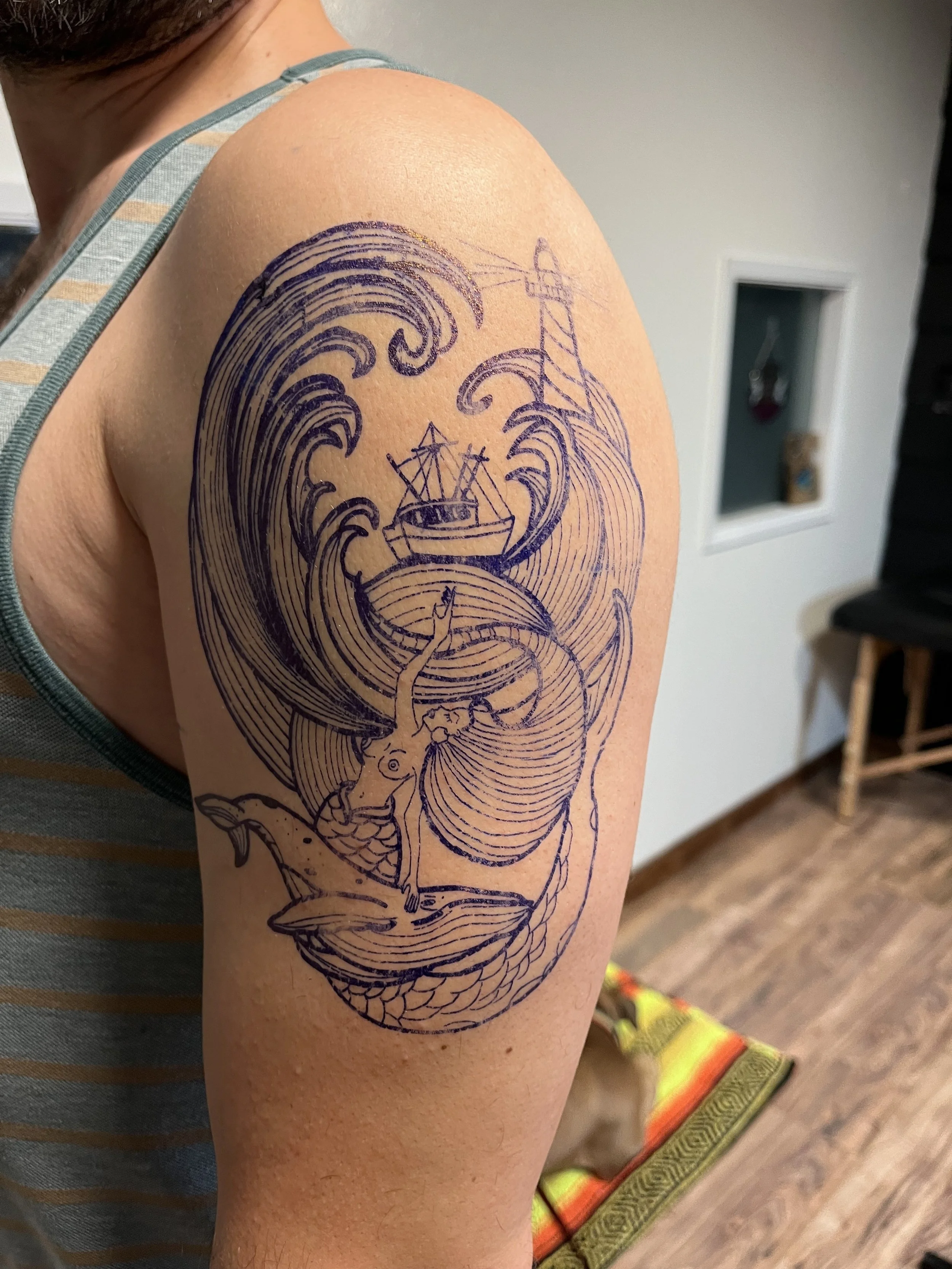 Temporary tattoo of a mermaid with a fish tail, surrounded by waves, a whale, a boat with a lighthouse, and a lighthouse in the background.