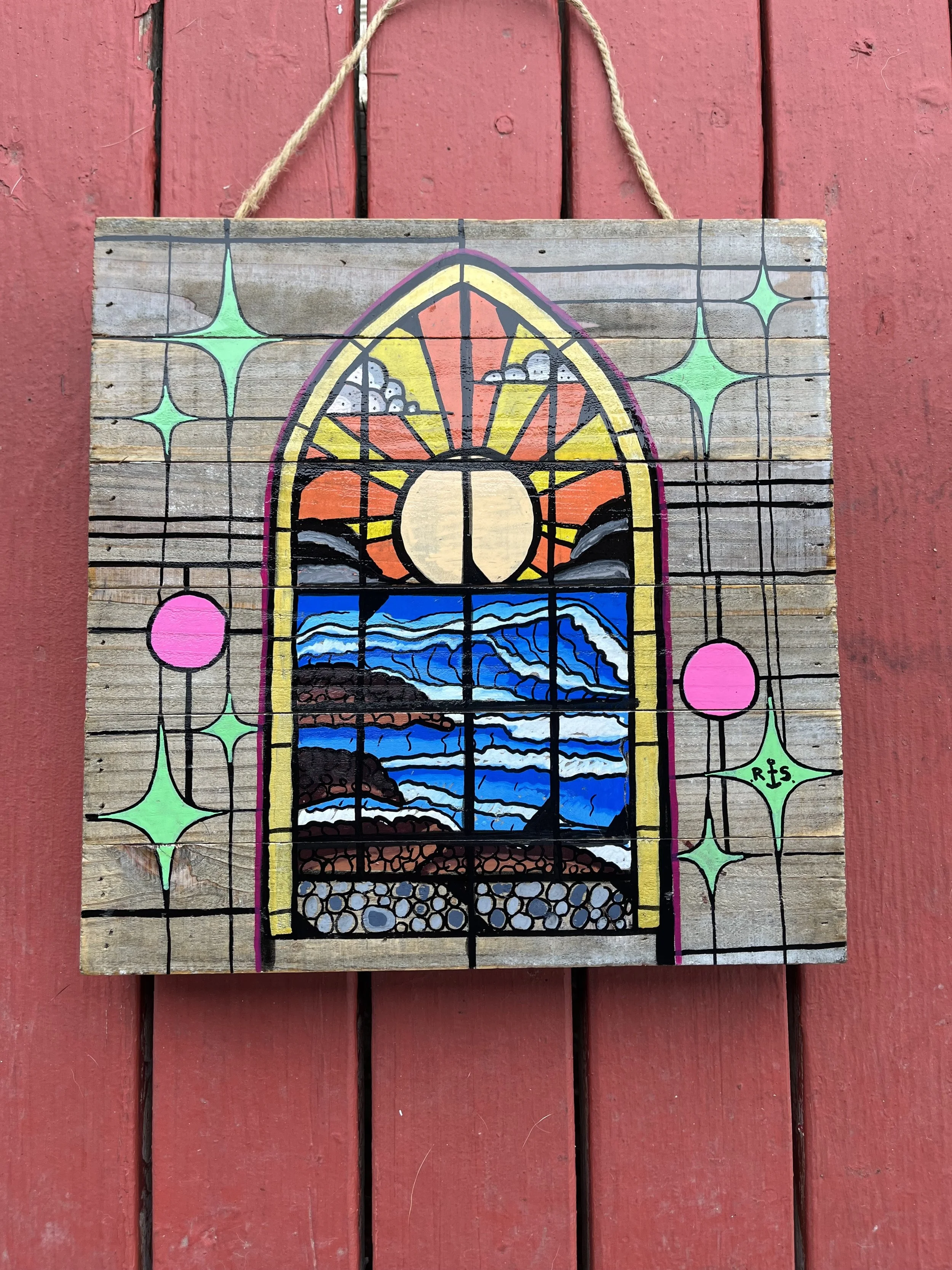 Painted wooden wall hanging depicting a stained glass window with a sunset over ocean waves, surrounded by colorful stars and circles. Signed 'RIS' in bottom right corner.