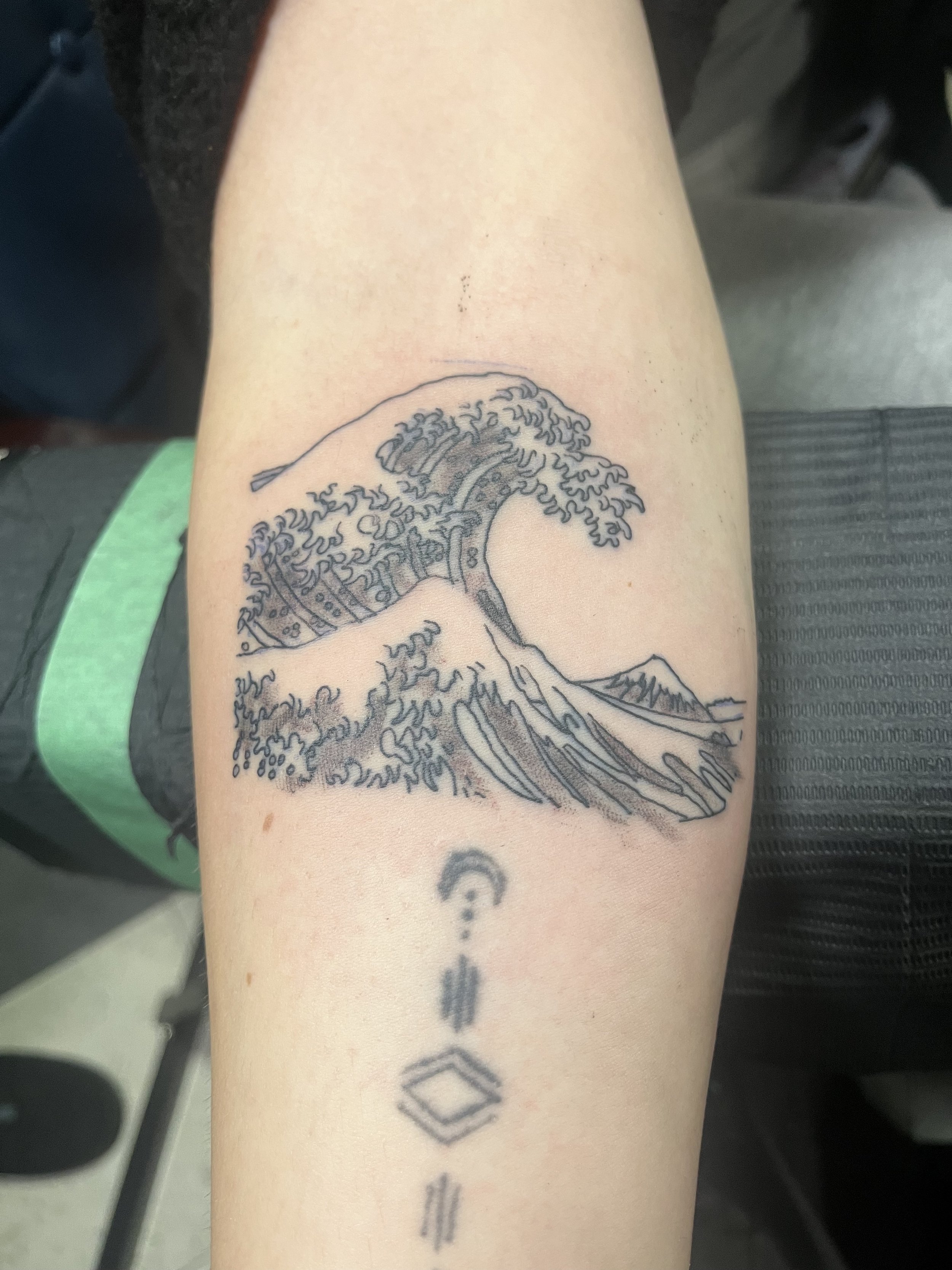 Tattoo of The Great Wave off Kanagawa on a person's forearm, with a smaller, abstract geometric design below it.