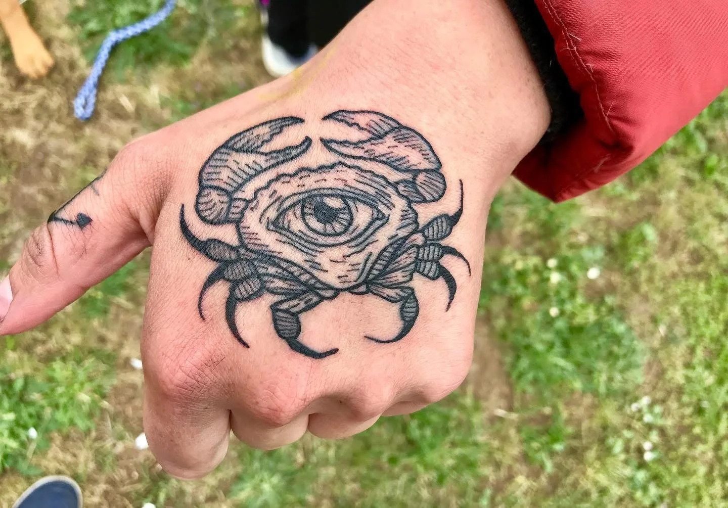 Tattoo of a crab with an eye in the center on a person's hand.