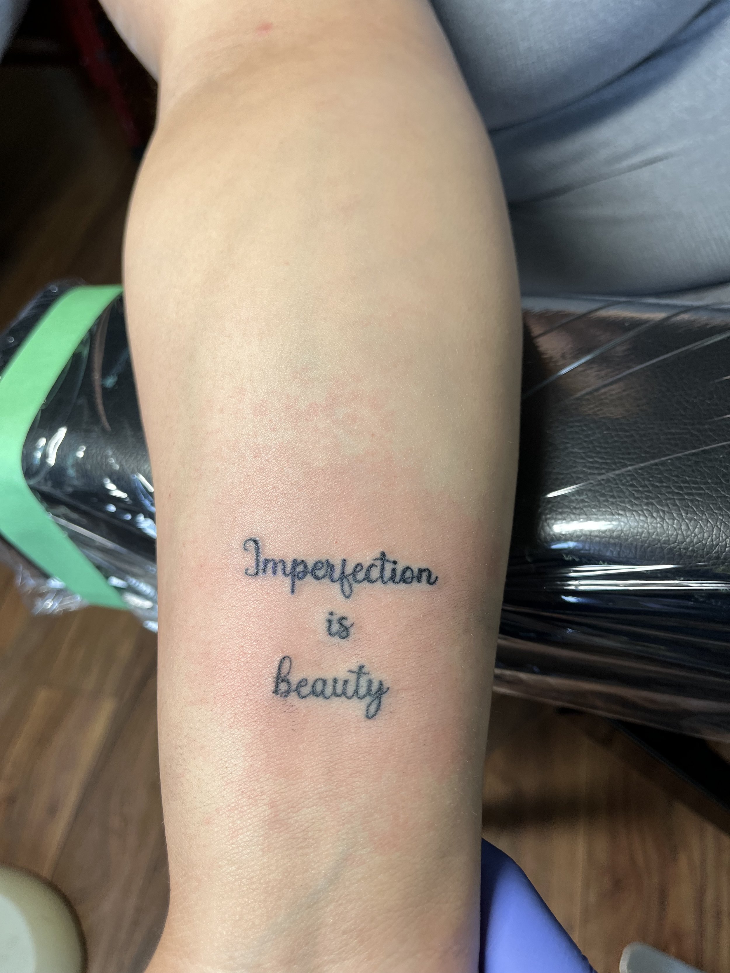 A tattoo on a person's forearm that reads 'Imperfecttion is beauty' in cursive font.