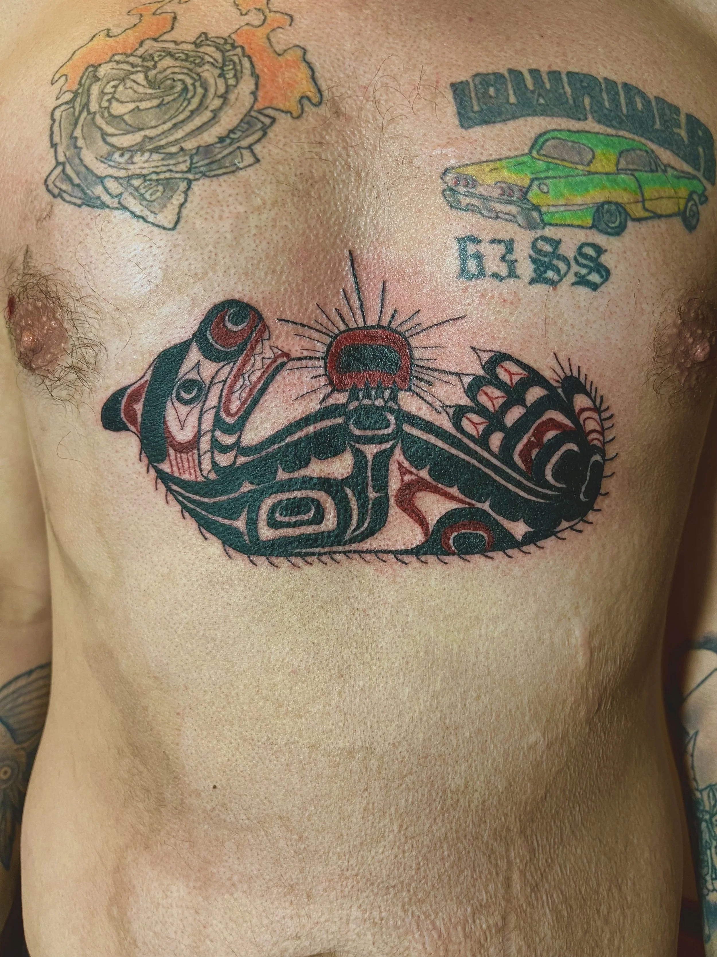 Tattoo of a stylized praying mantis on man's chest, with additional tattoos of a rose, a vintage car, and a text band.