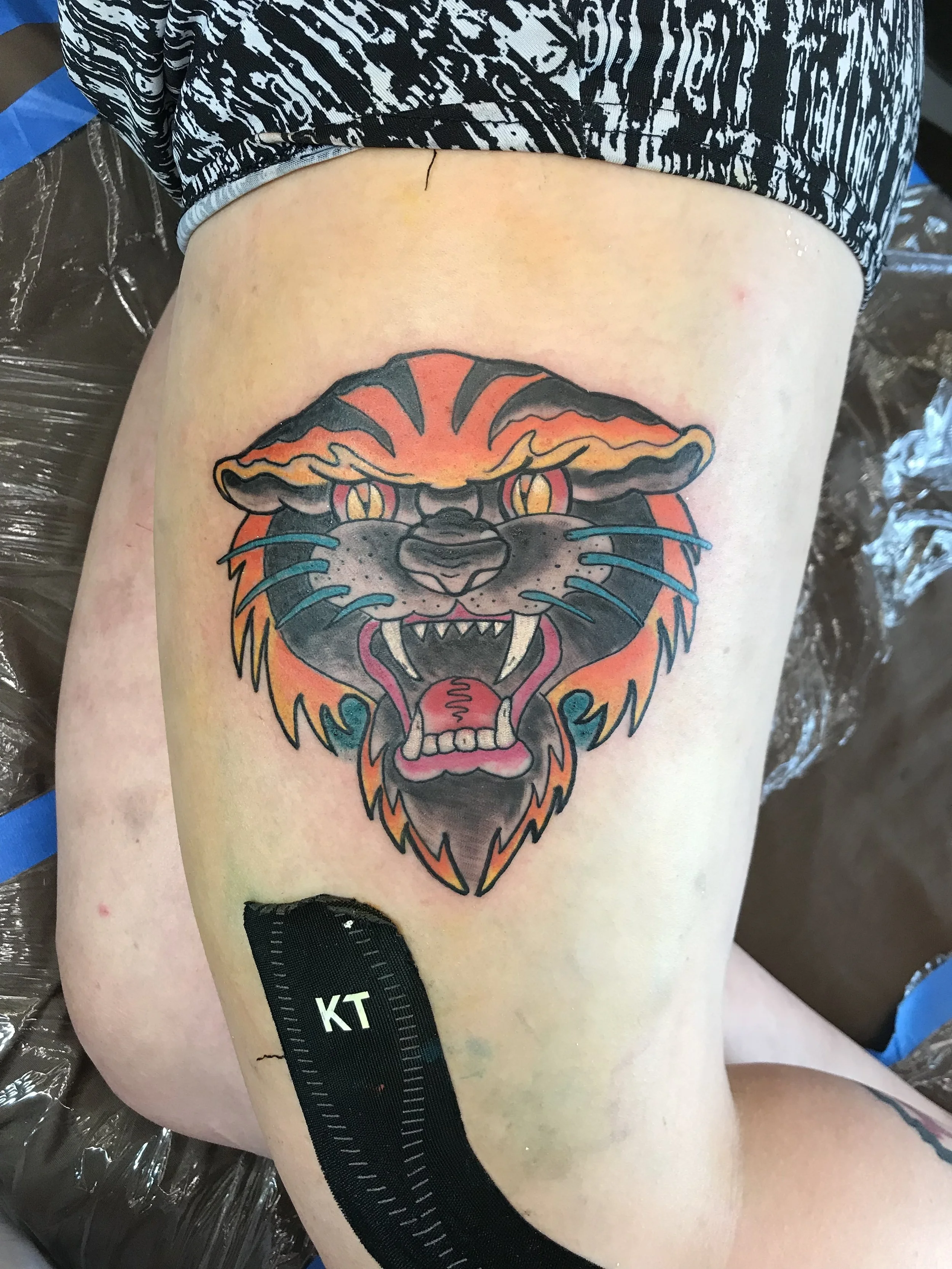 Colorful tattoo of a fierce lion's face on a person's thigh.