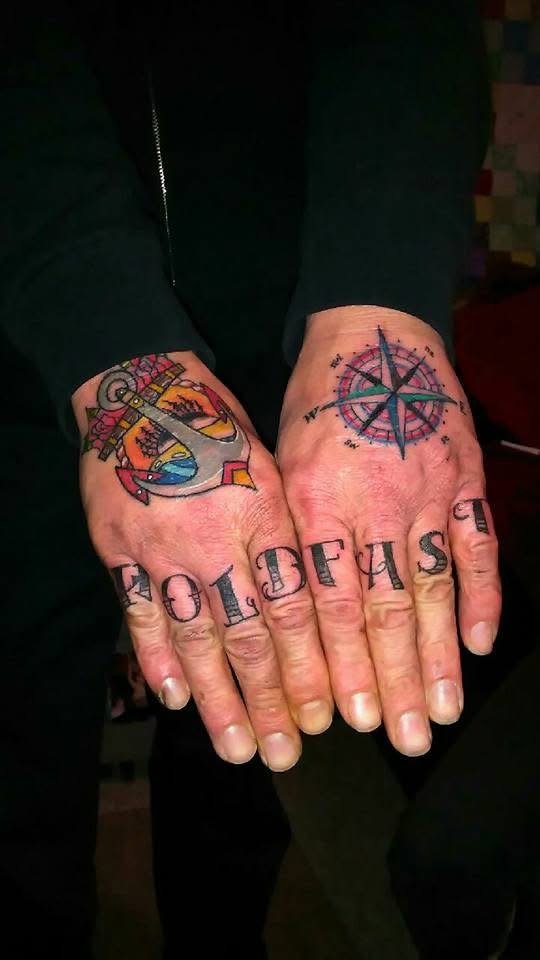 Hand tattoos displaying the word "LOVELY" on fingers, a colorful anchor, and a compass rose.