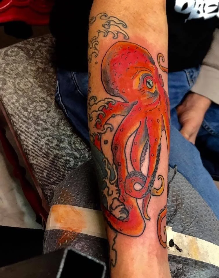 Tattoo of an orange octopus on a person's forearm with swirling water patterns around it.