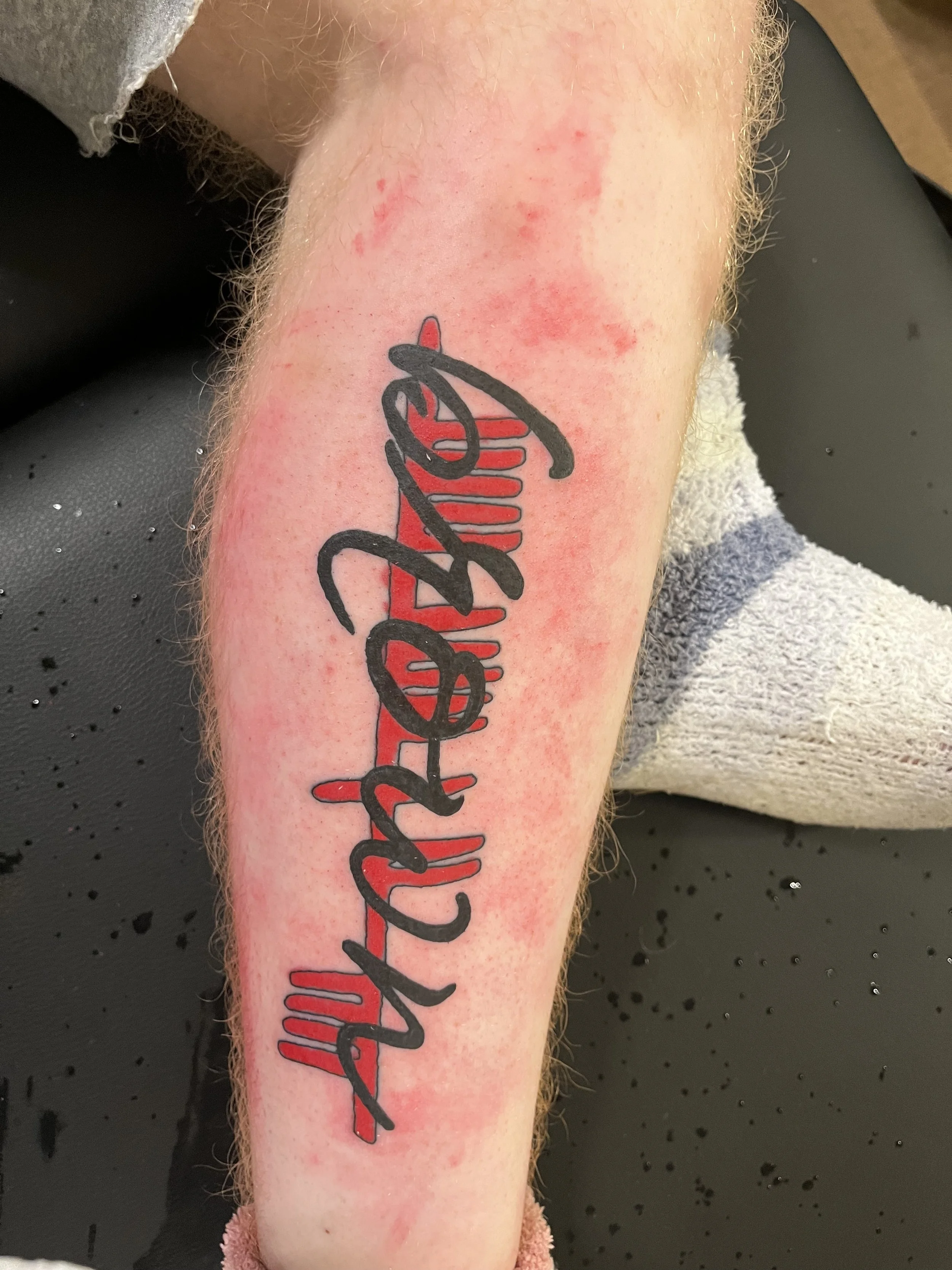 Fresh tattoo of the name 'William' in black cursive with a red background design on a person's forearm.
