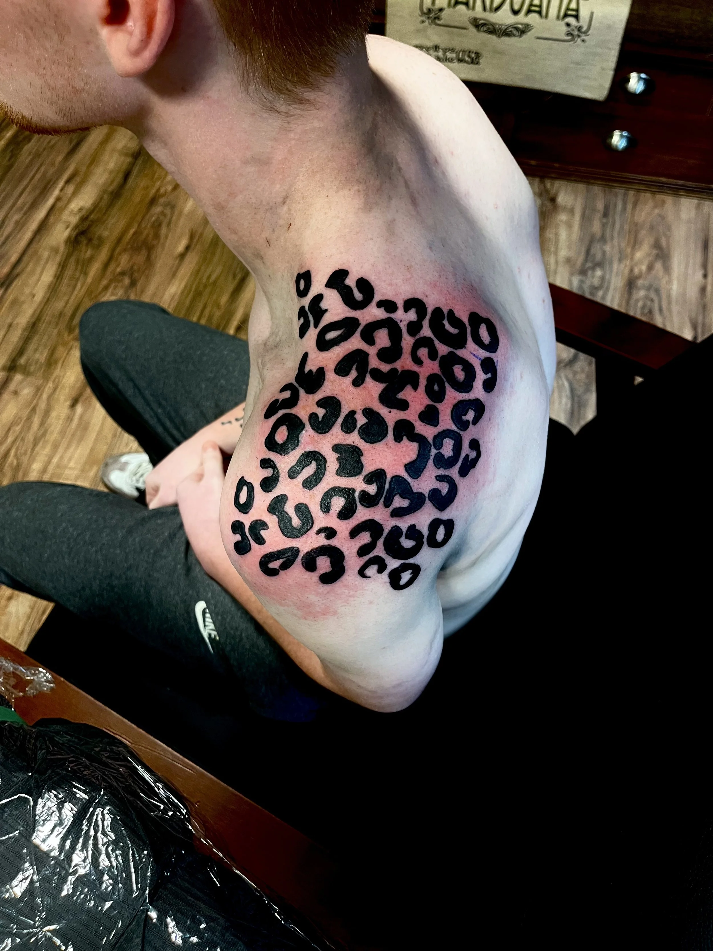Tattoo of a black leopard pattern on a person's shoulder, with reddish skin around the tattoo.