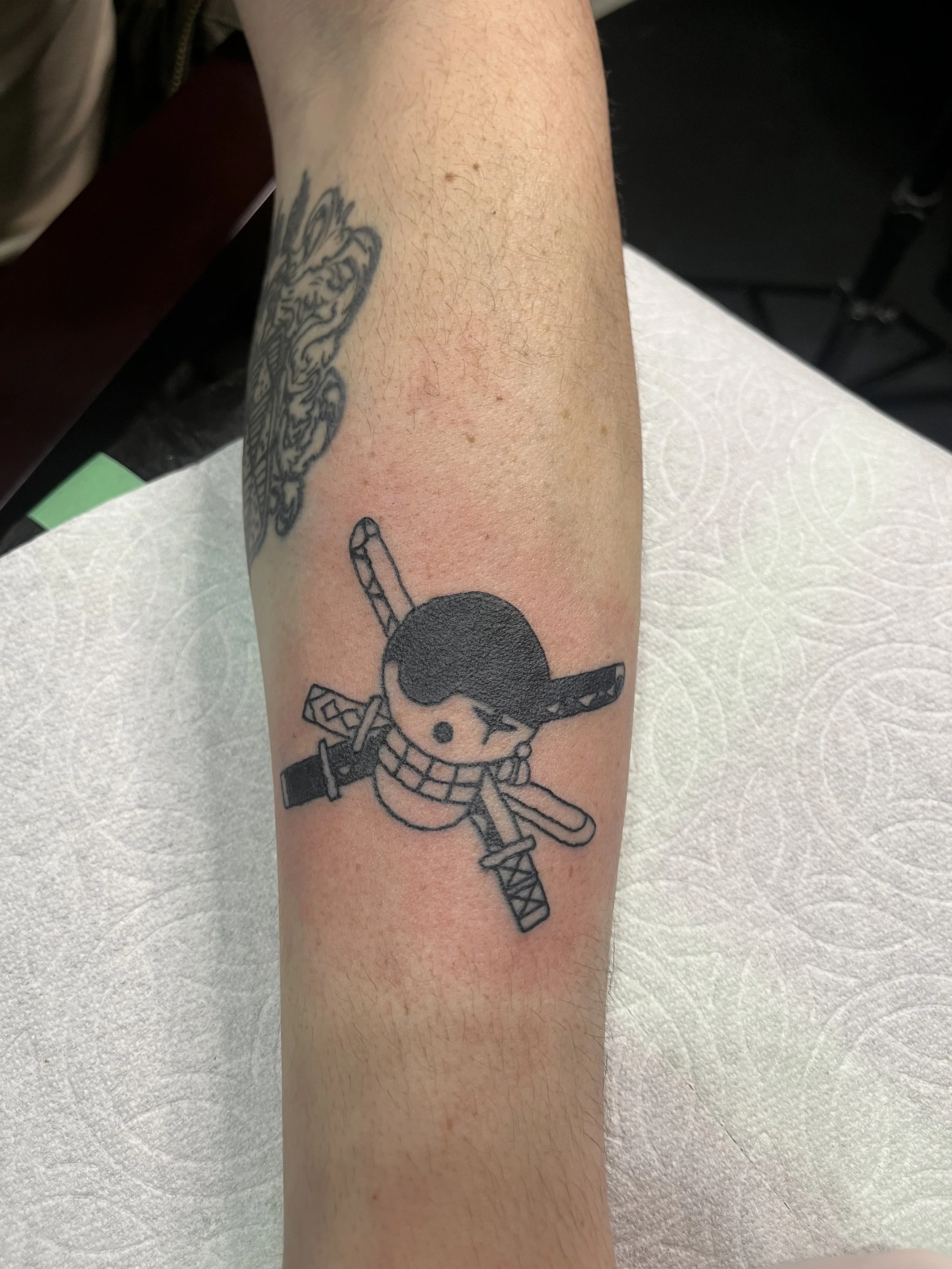 Tattoo of a cute cartoon ninja with a sword on a person's forearm.