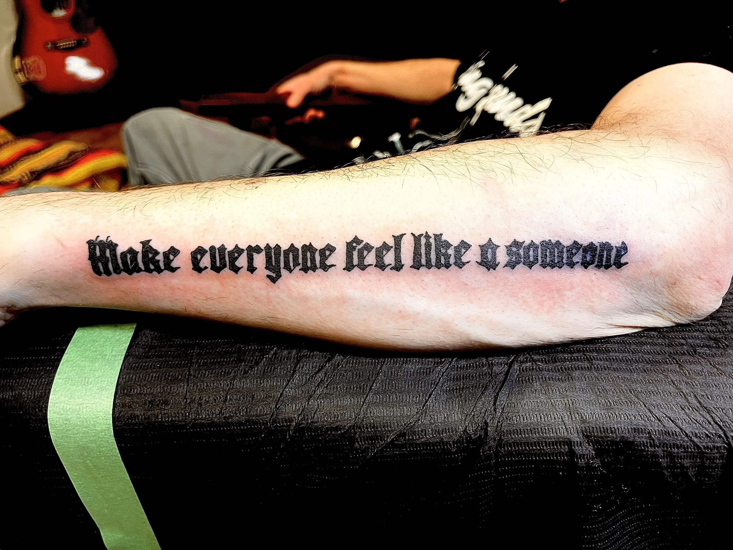 Tattoo on person's forearm that reads, 'make everyone feel like a someone,' in black Gothic font.