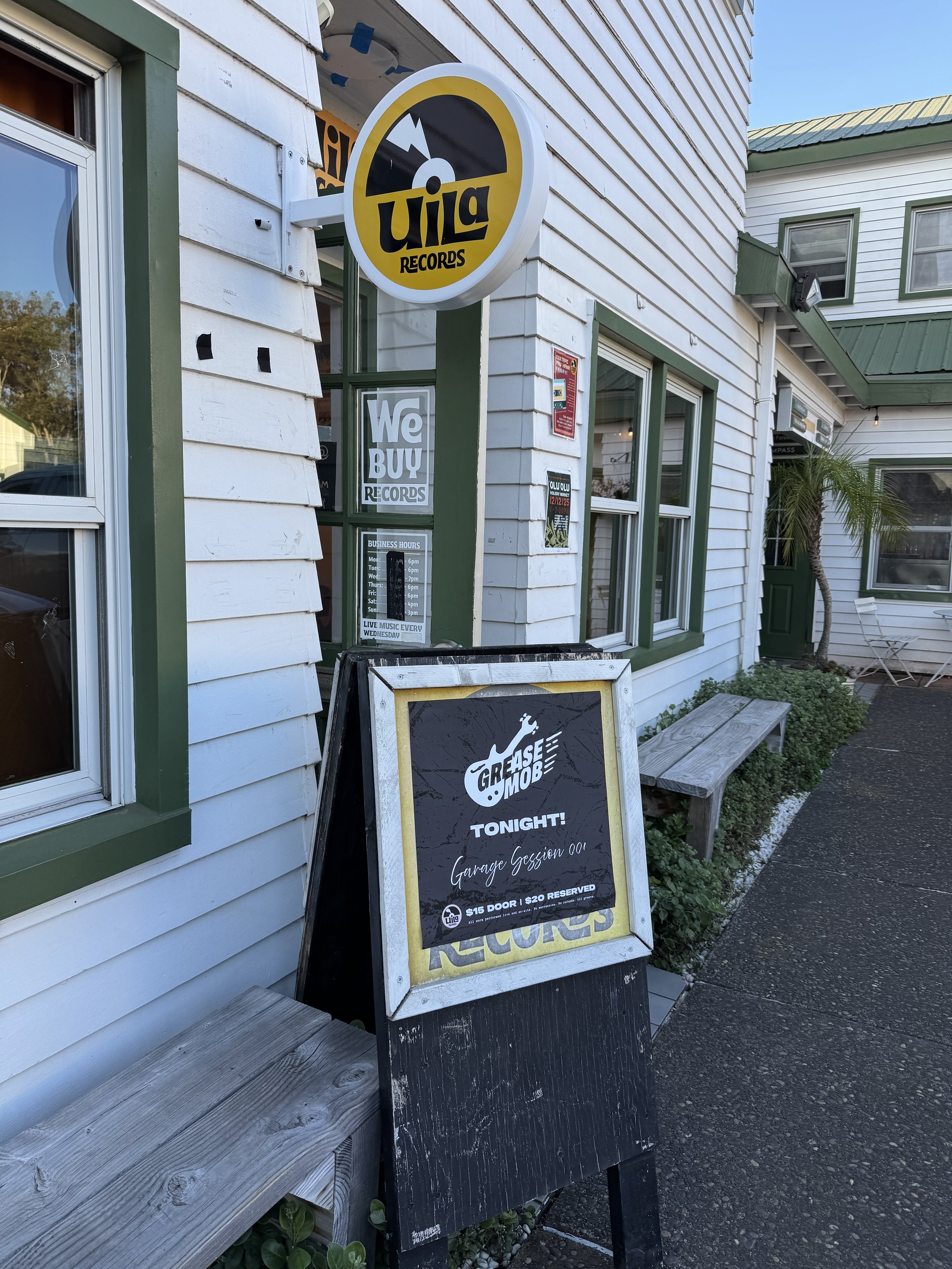Sign outside a shop advertising a Garage Gession DJ event tonight, with a blackboard sign mentioning $15 door and $20 reserved, in front of a white building with green trim and a bench.