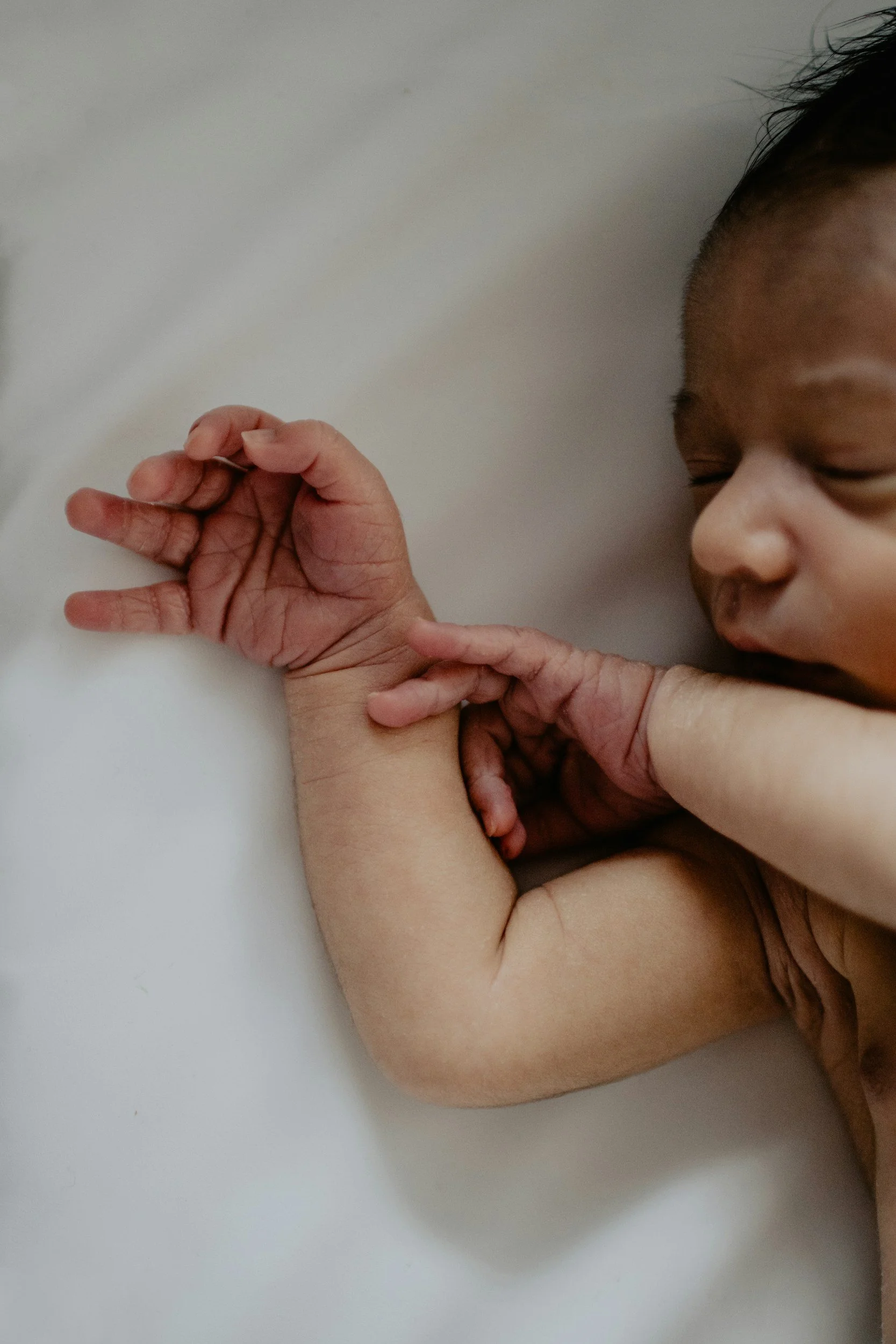 Close-up of a baby sleeping with adult hand gently touching the baby's arm.