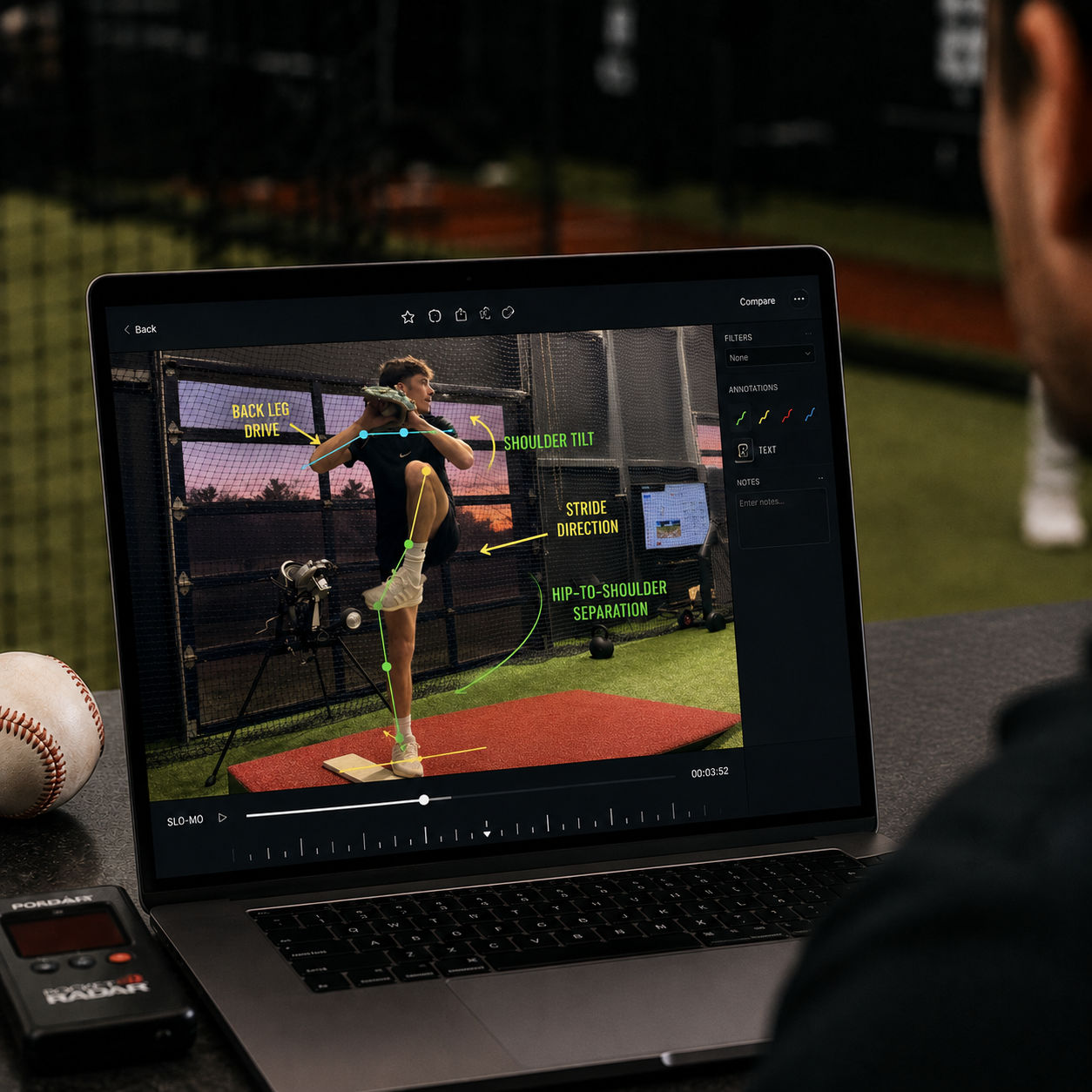 Person analyzing baseball pitching biomechanics on a laptop, with annotations like shoulder tilt and hip-to-shoulder separation, at a training facility.