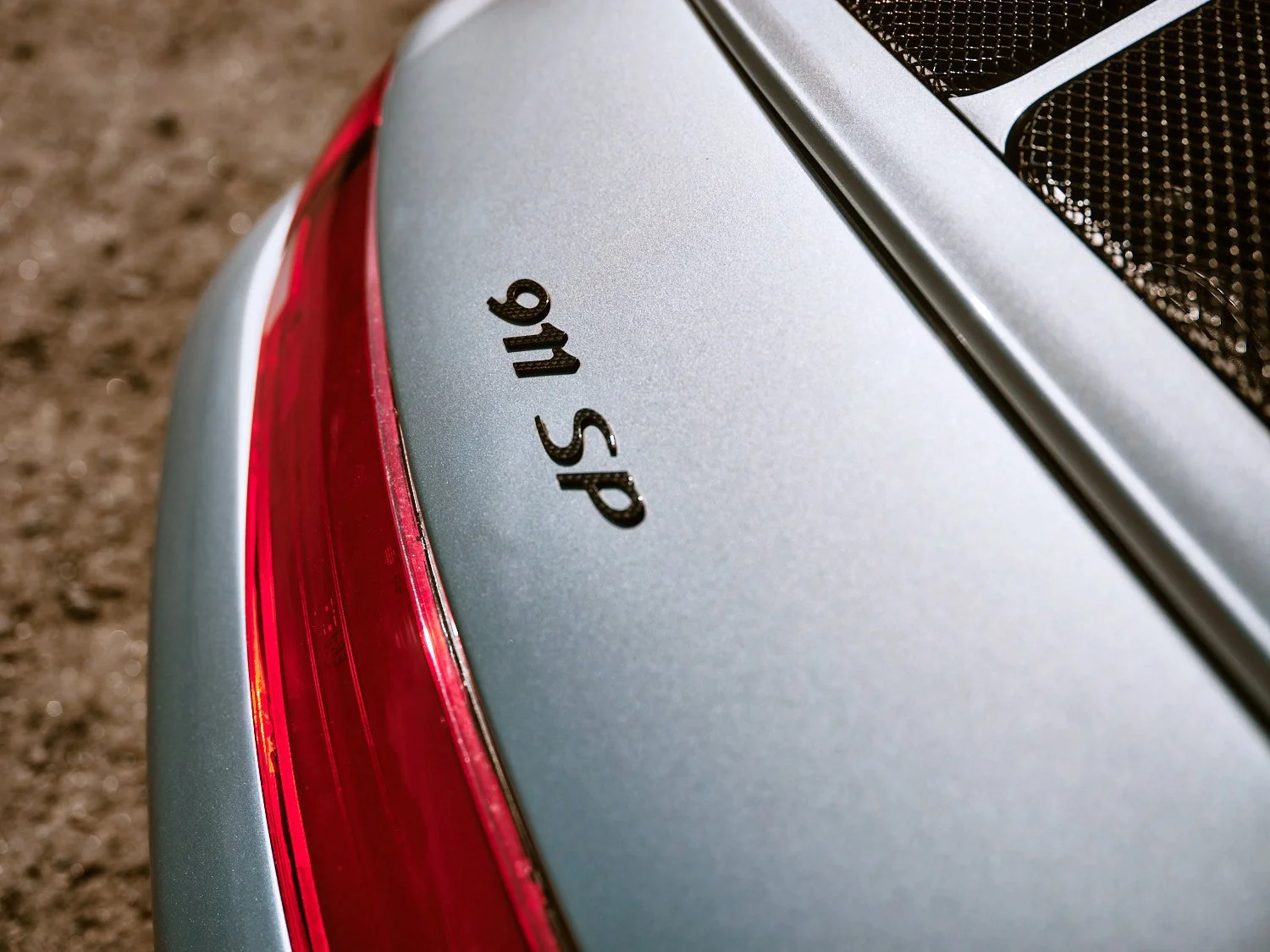 Close-up of a silver car's rear with black 'SP 16' badge and red tail light.