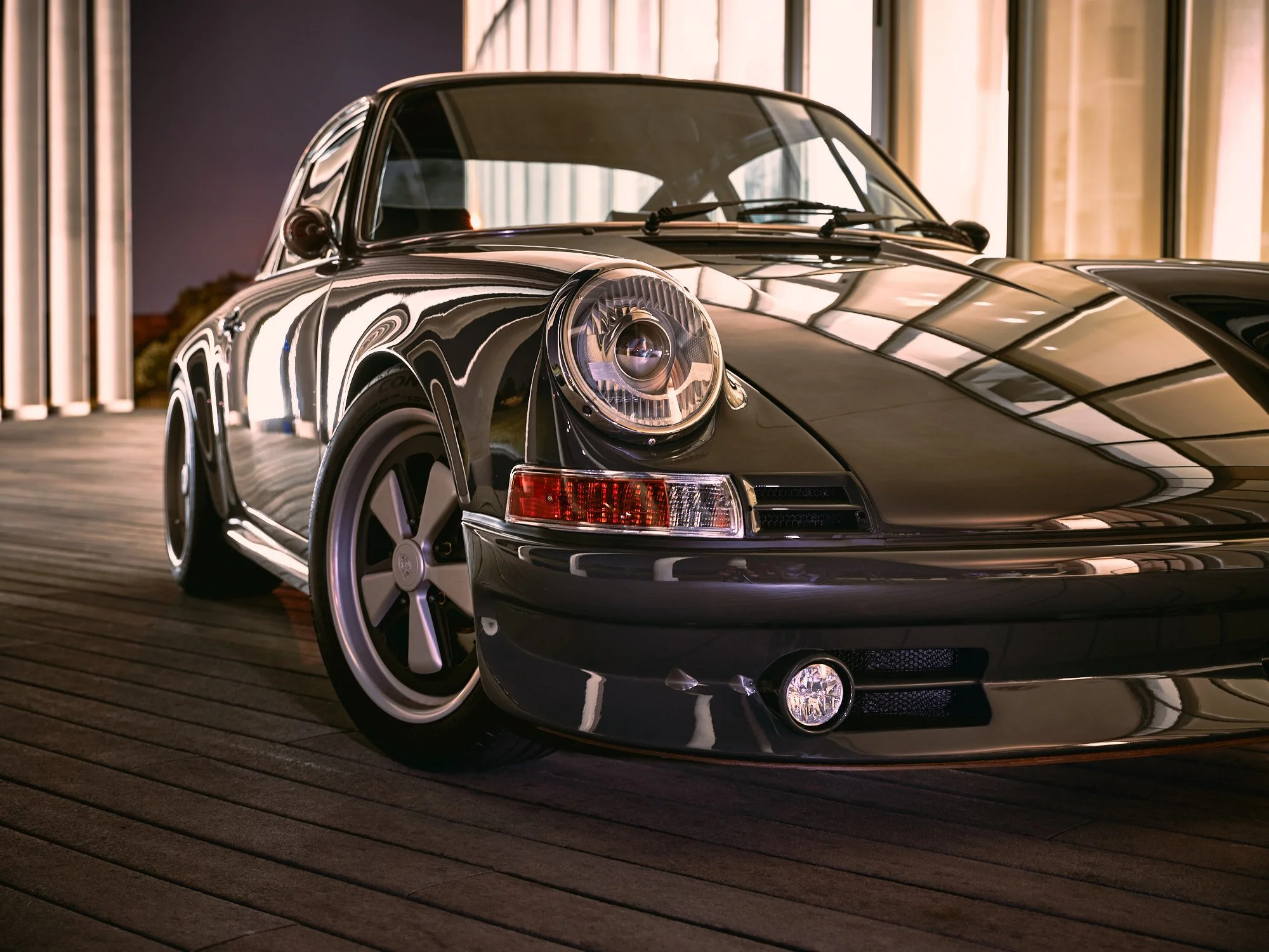 A classic black Porsche sports car parked indoors with reflections on its shiny surface and a wooden floor.