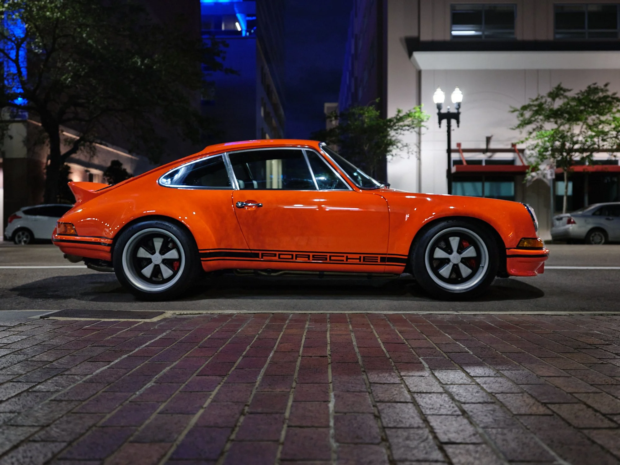 A classic orange Porsche sports car parked on a city street at night.