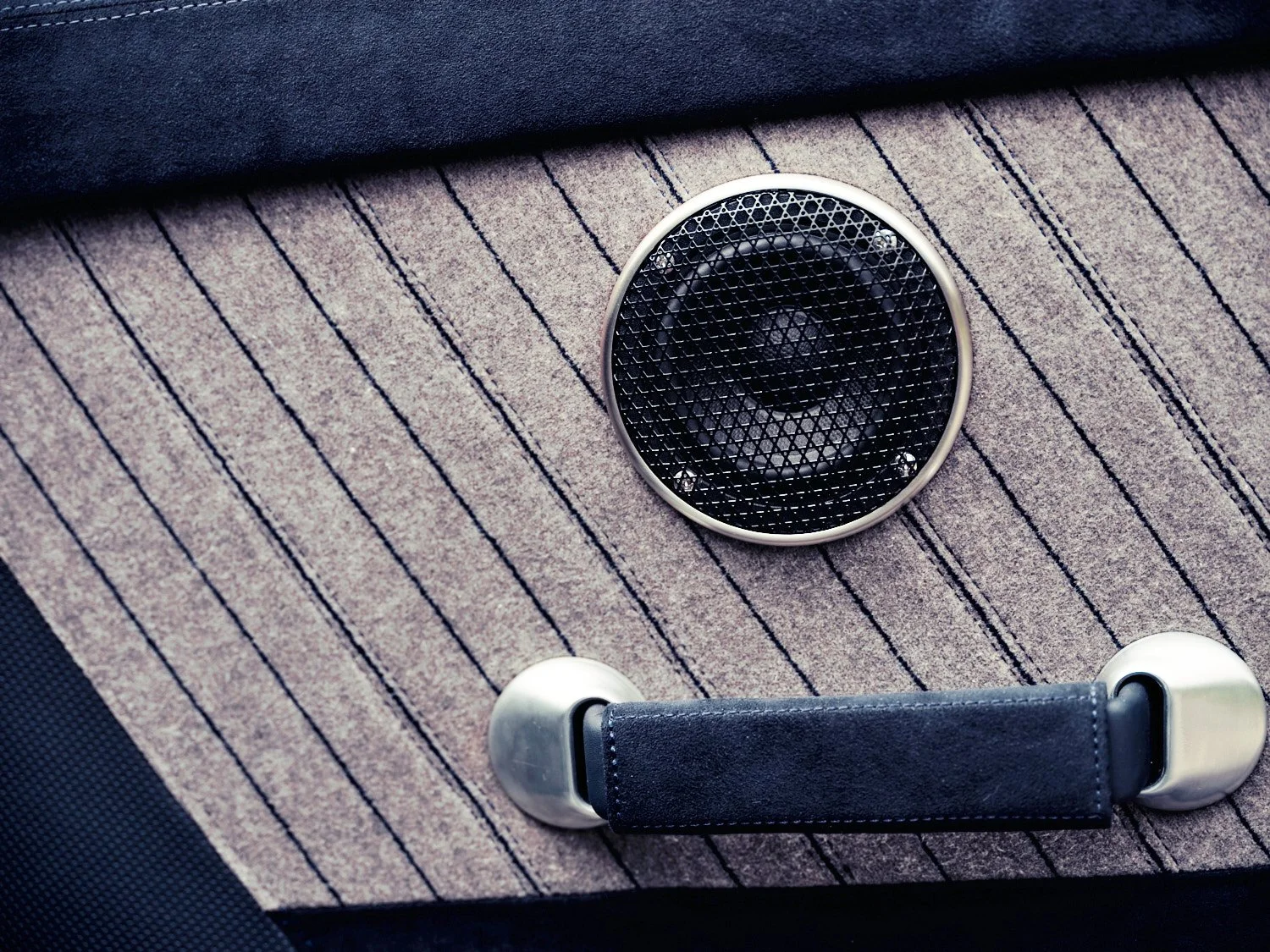 A small round speaker and a black handle on a textured beige striped fabric surface.