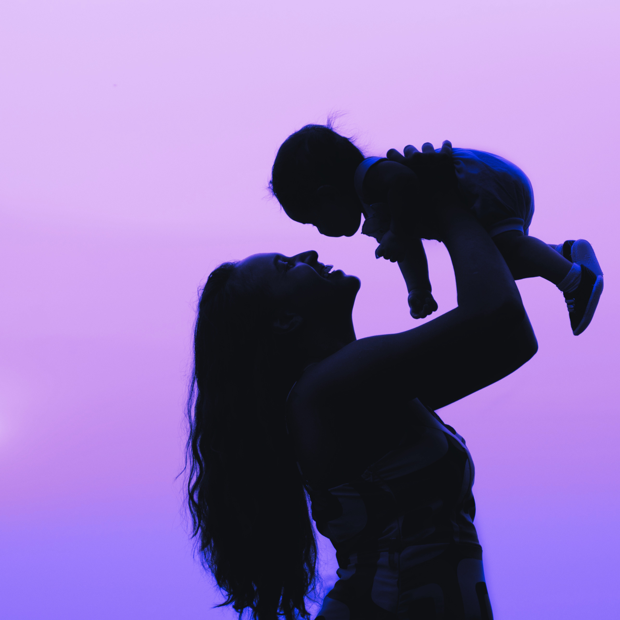 Silhouette of a woman lifting a child in the air against a purple background.