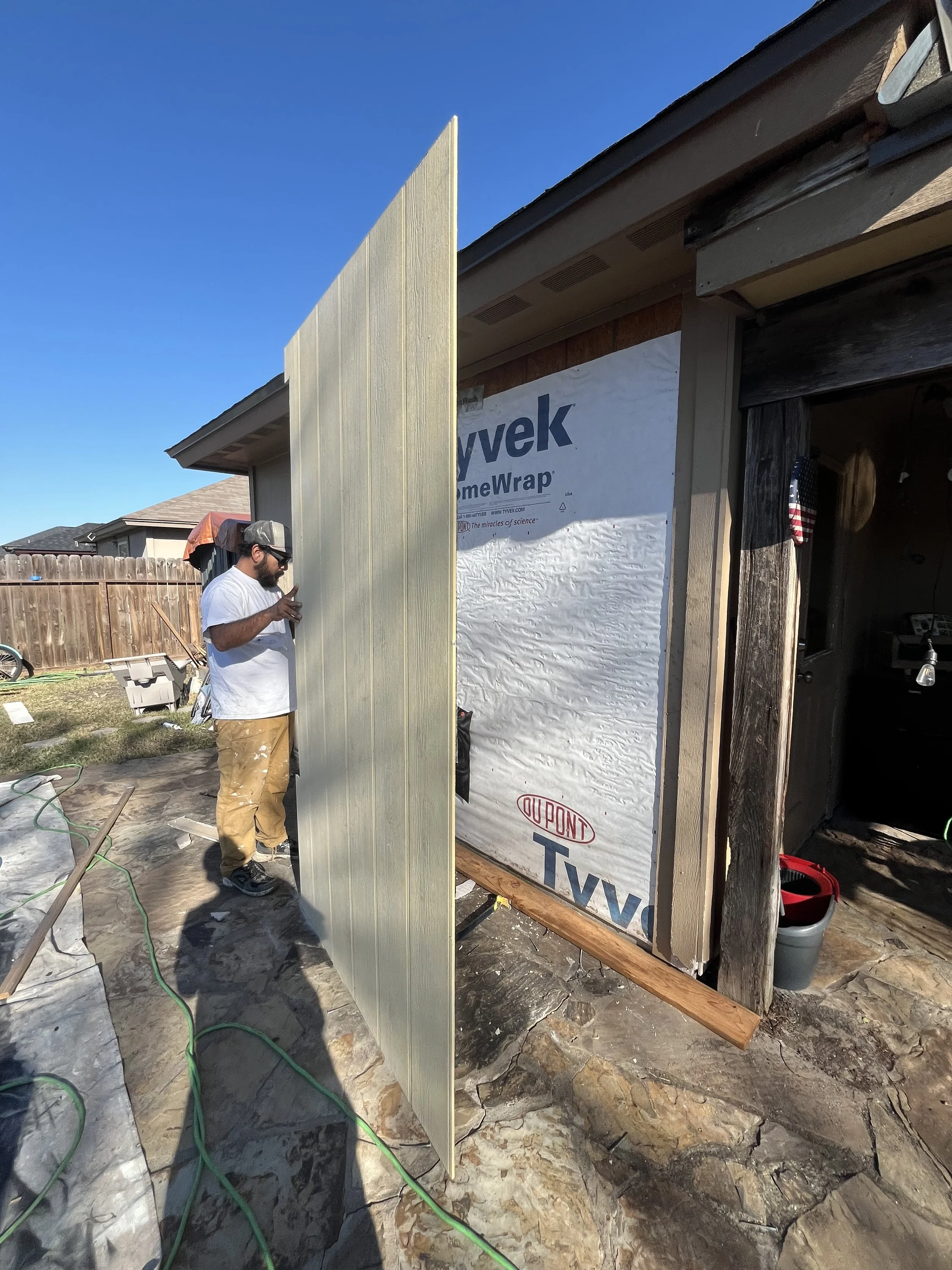 Man installing or working on a vertical siding panel on a house exterior during daytime.