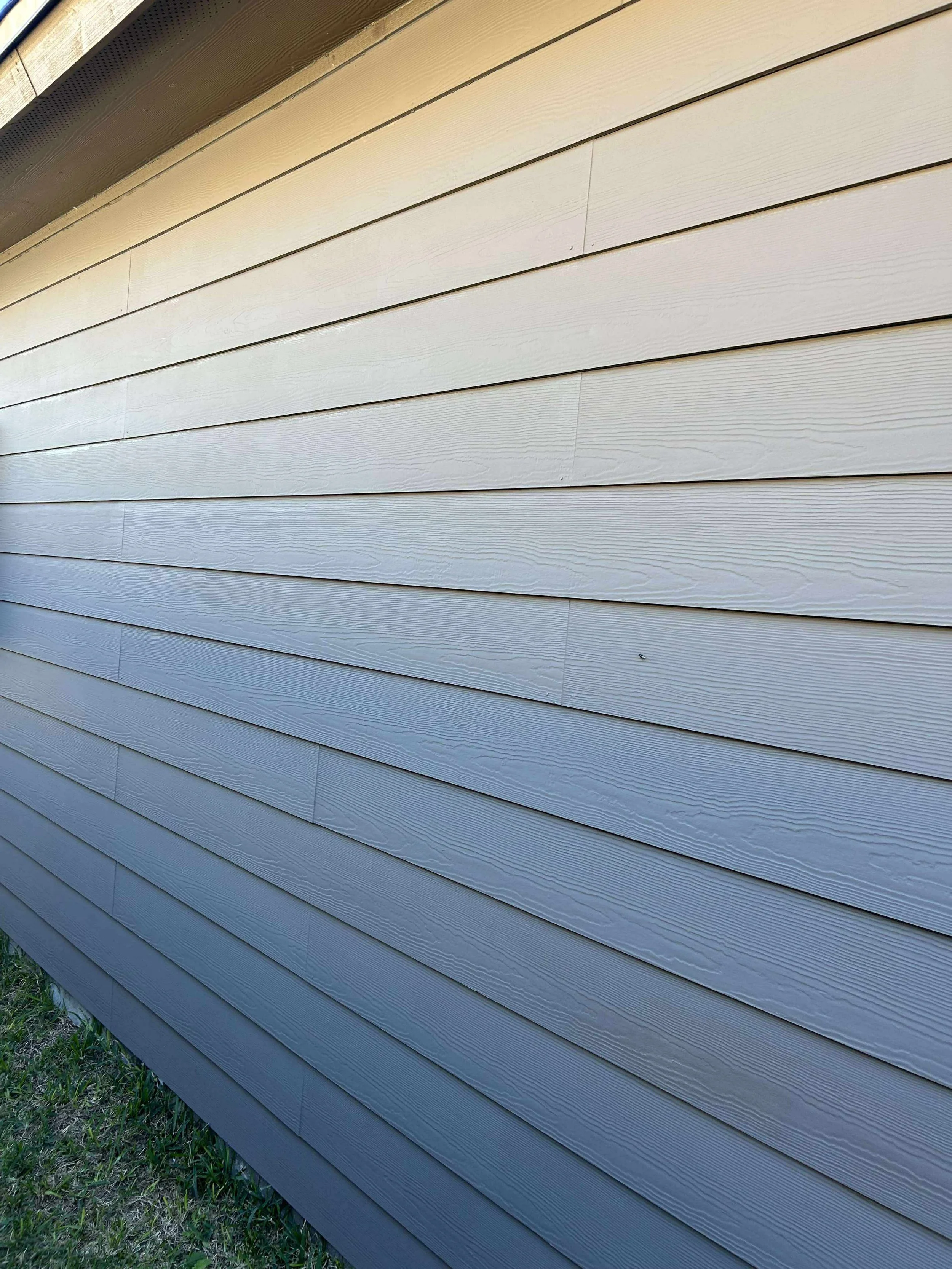 Close-up of beige horizontal siding on a building with grass at the bottom edge.