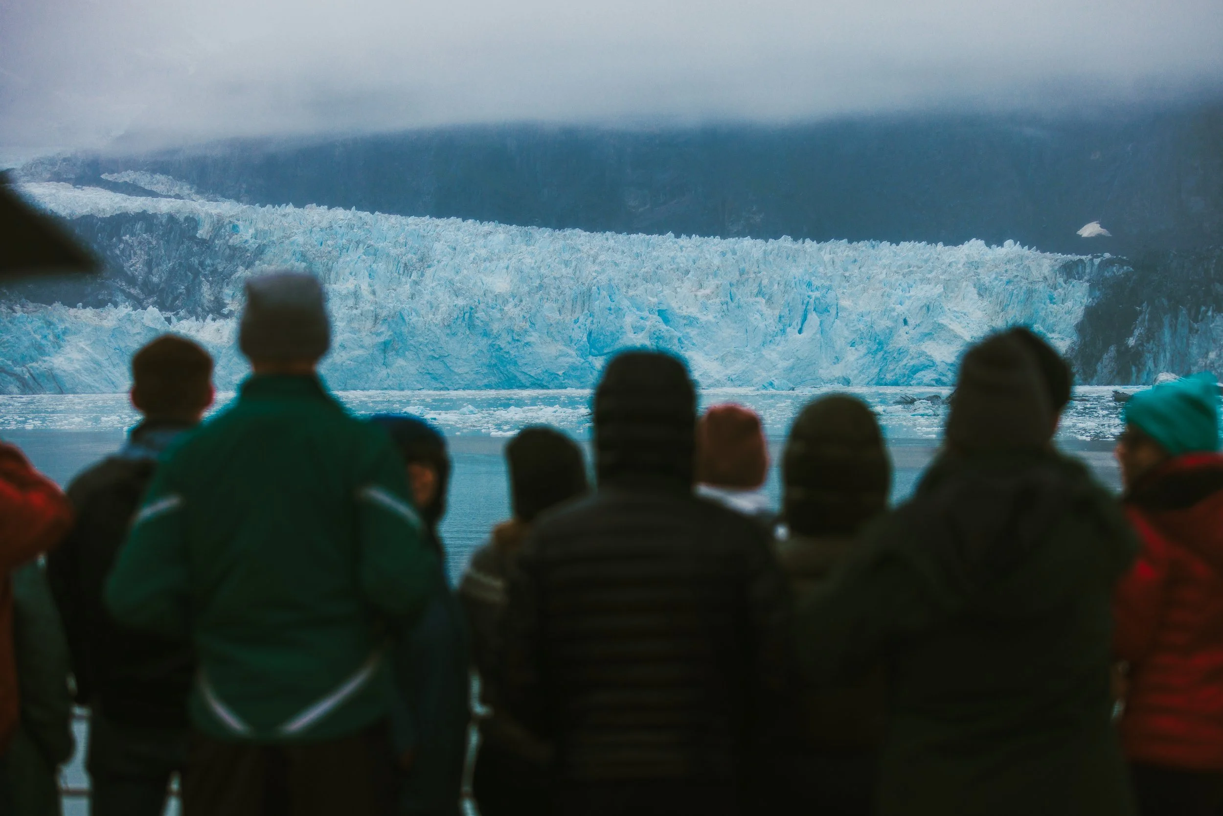 People viewing a glacier in a cold, overcast environment.