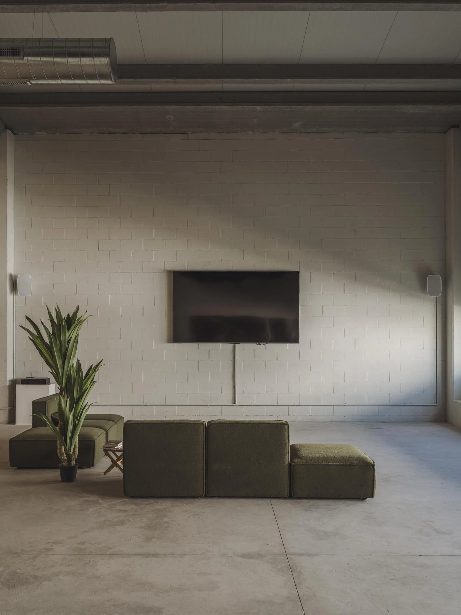Sala moderna con sillones verdes, planta y televisor montado en pared blanca de ladrillos.