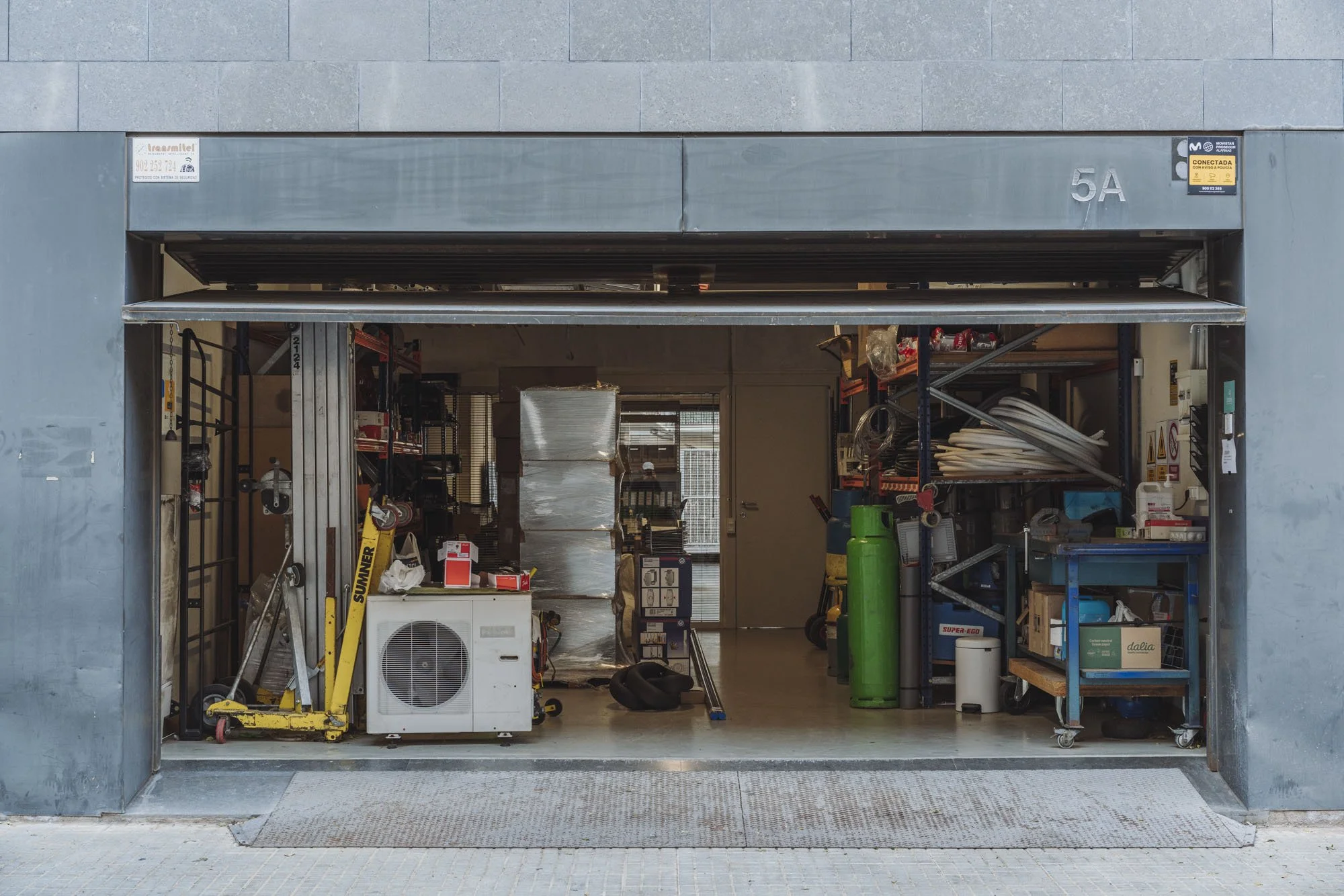 Vista frontal de un garaje abierto con herramientas, equipos y materiales de construcción en su interior.