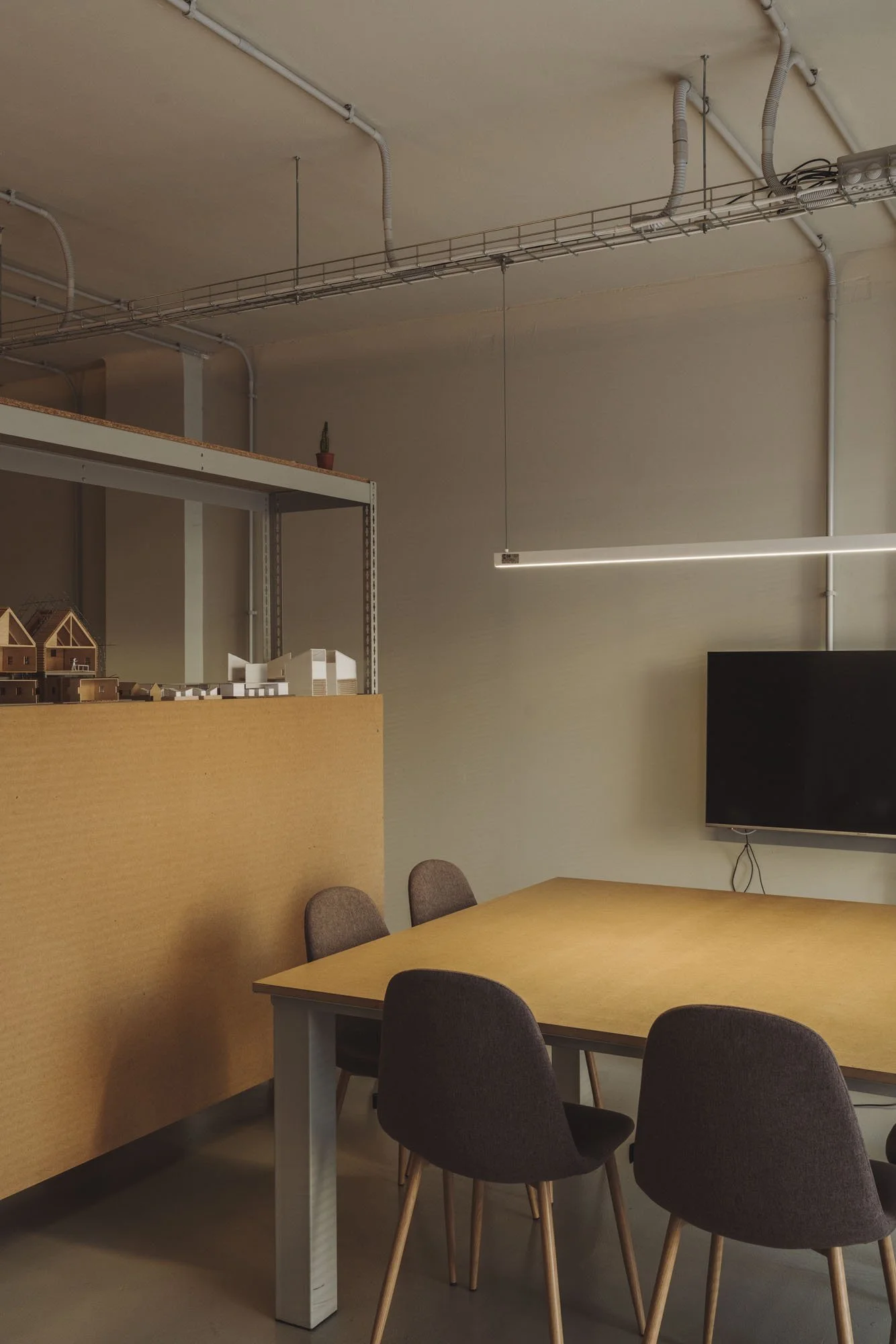Sala de reuniones con mesa de madera, sillas oscuras, una pantalla plana negra y estantería con modelos en miniatura.