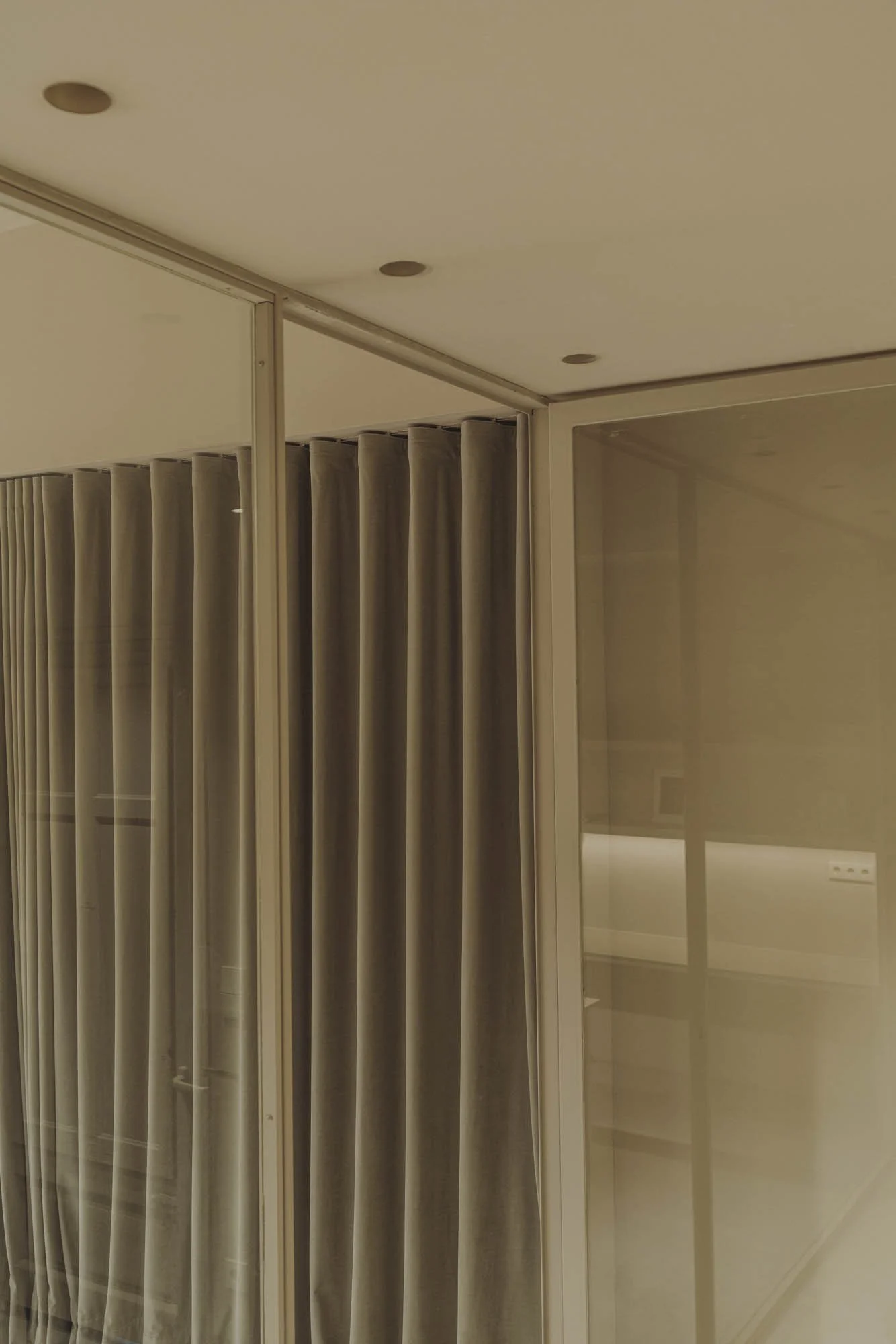 Imagen de un interior con cortinas beige y ventanas de vidrio con marco blanco.